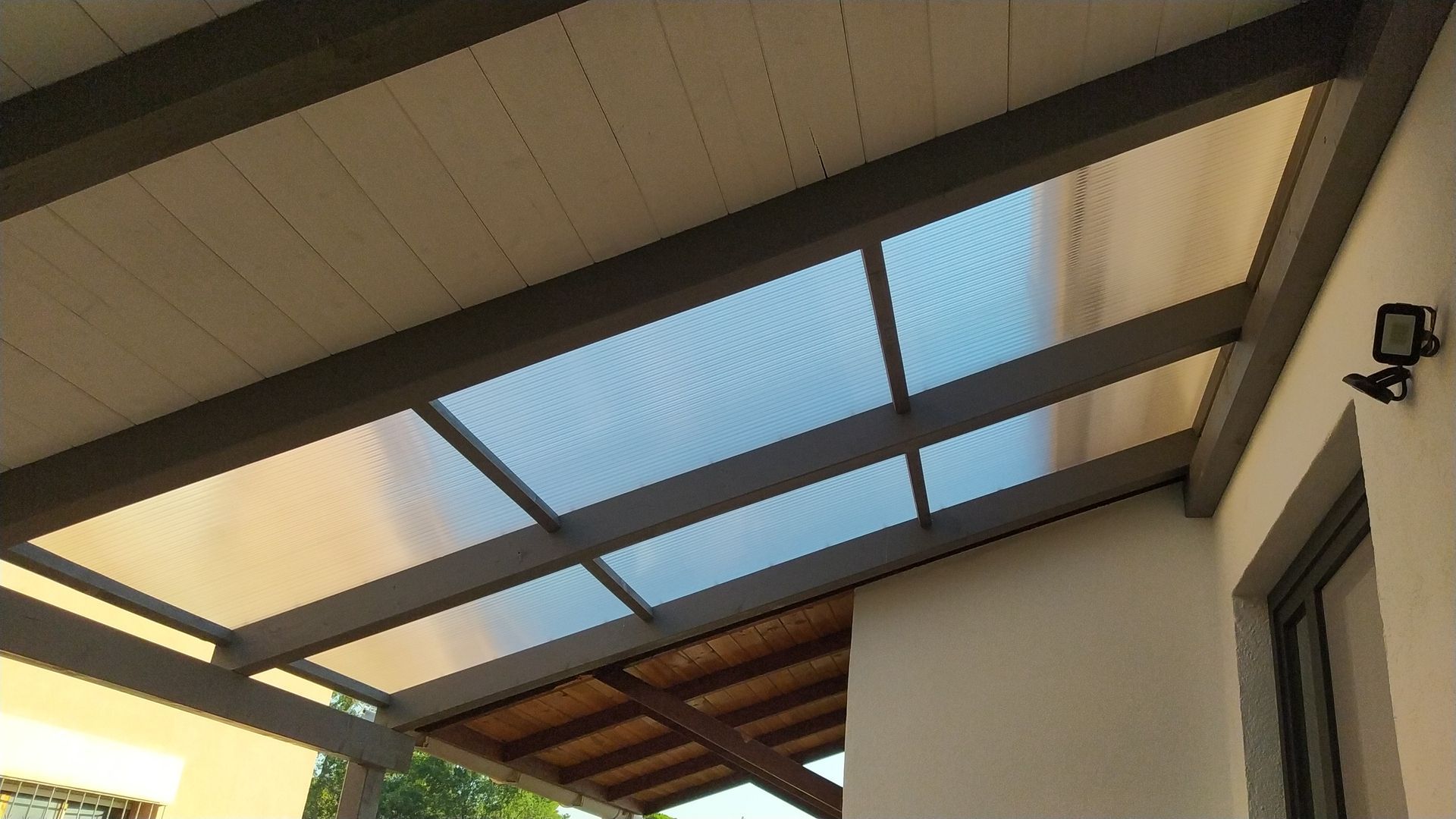 Una pérgola con techo transparente y una luz en el lateral de un edificio.