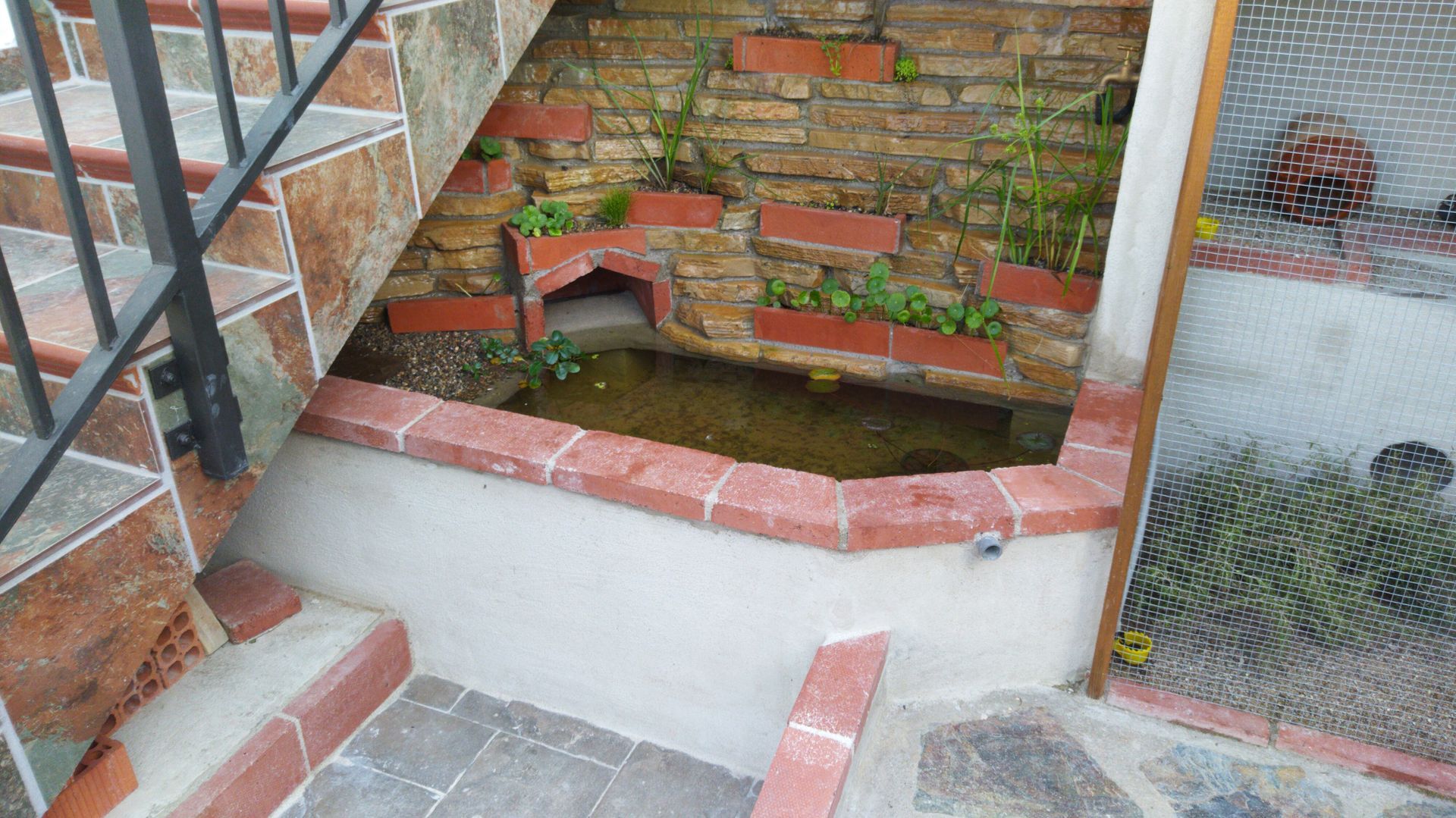 Un pequeño estanque en la esquina de un edificio al lado de unas escaleras.
