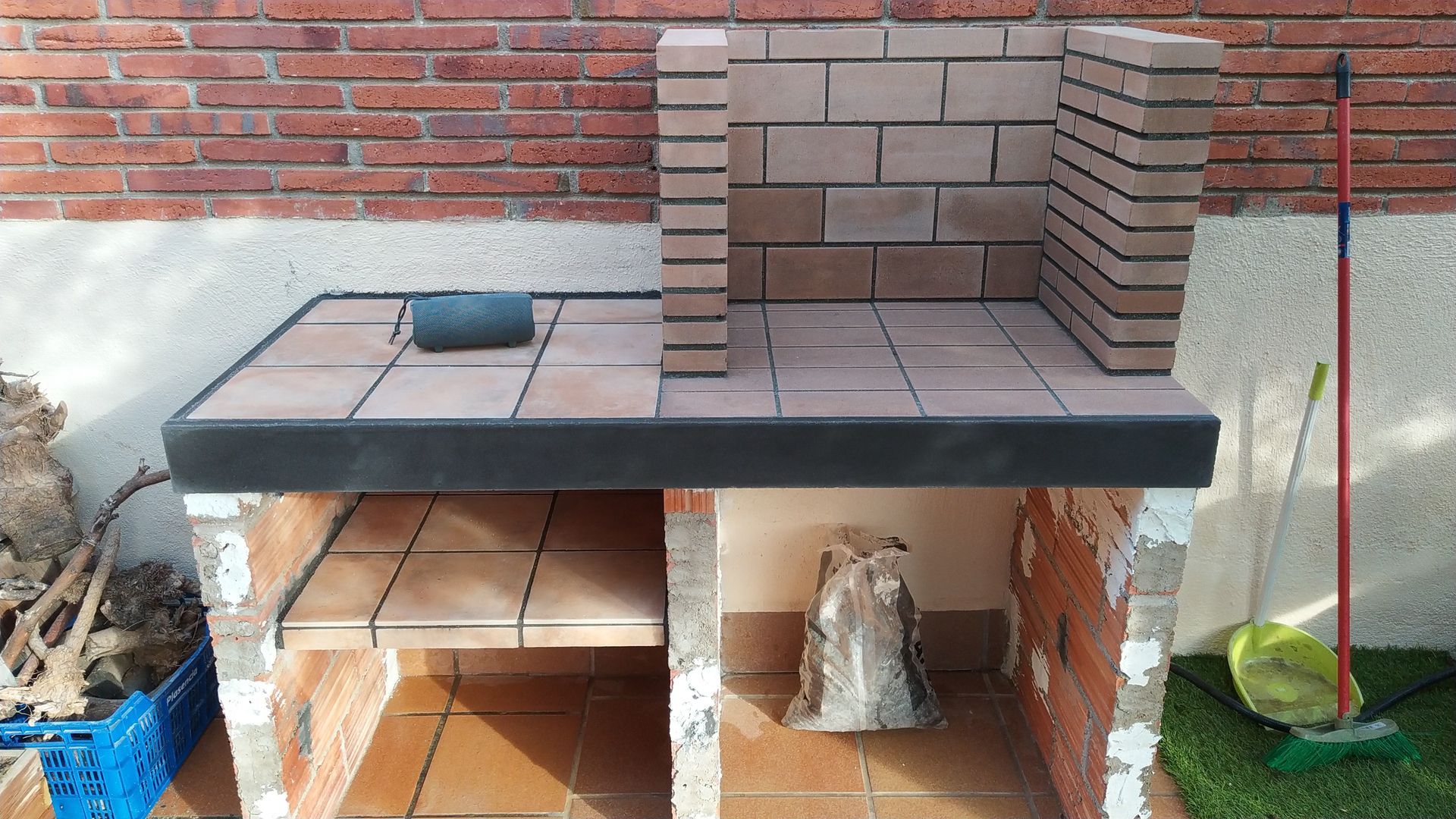 Una escoba está sentada en el césped al lado de una pared de ladrillos.