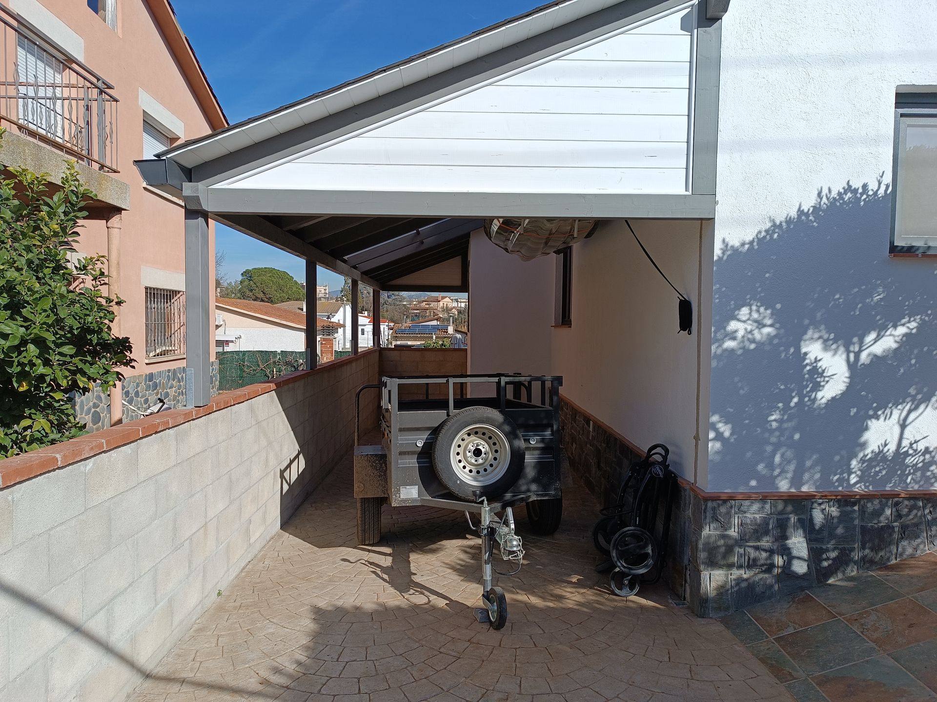Un remolque está estacionado bajo un toldo frente a una casa.