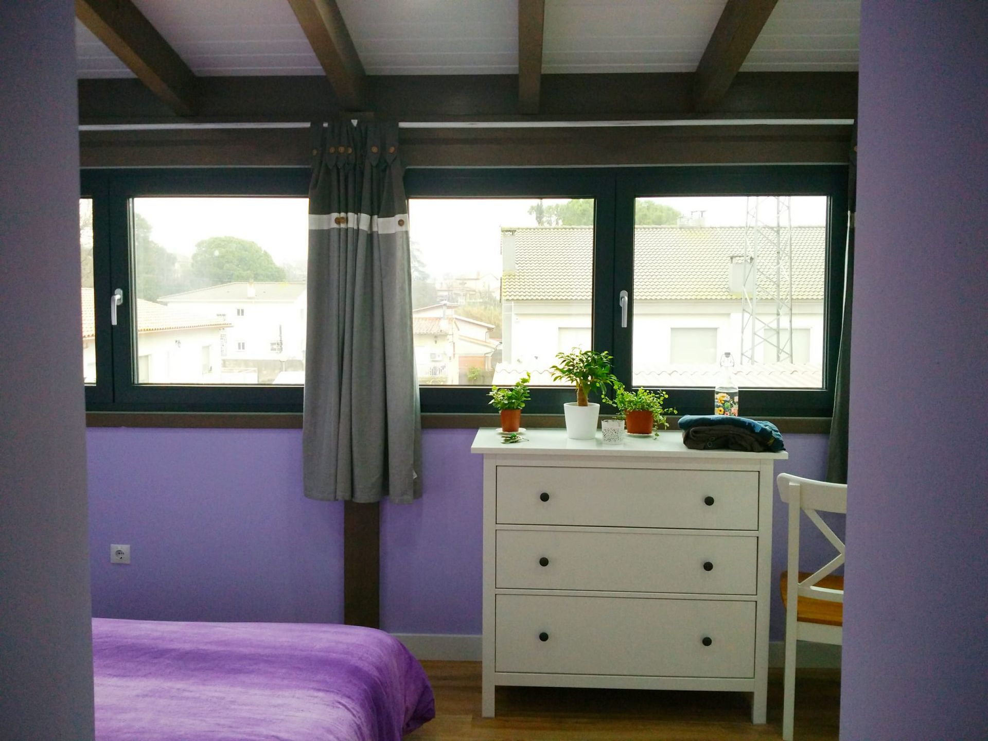 Un dormitorio con paredes moradas y una cómoda blanca.