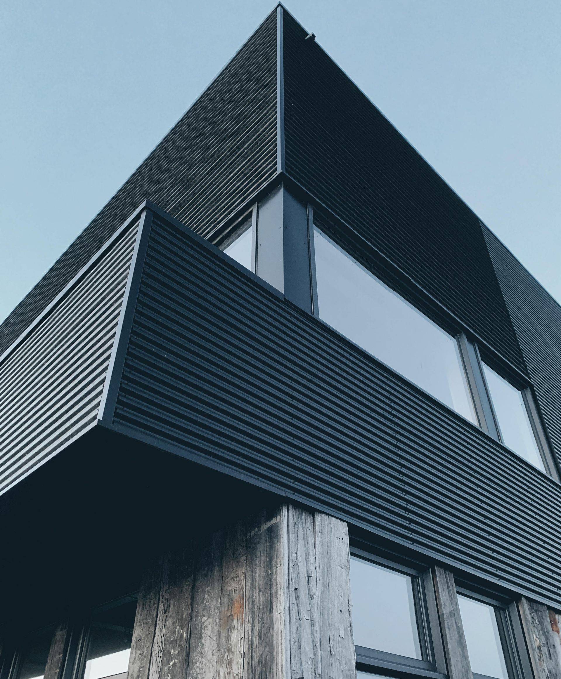 Extérieur moderne et angulaire noir du bâtiment avec de grandes fenêtres et une charpente en bois patiné
