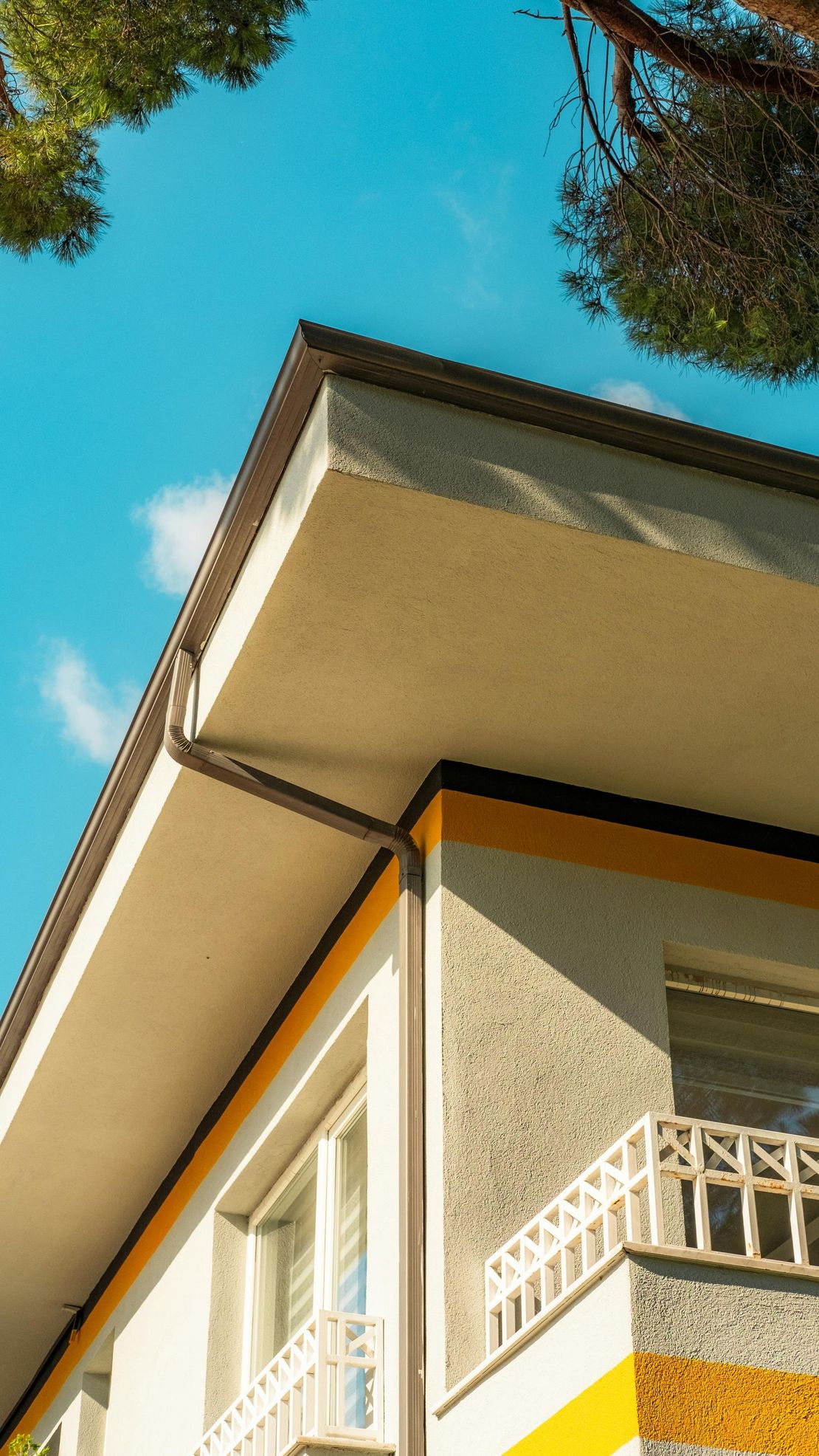 Coin d'un immeuble beige avec des balustrades de balcon blanches se détachant sur un ciel bleu vif et des branches d'arbres
