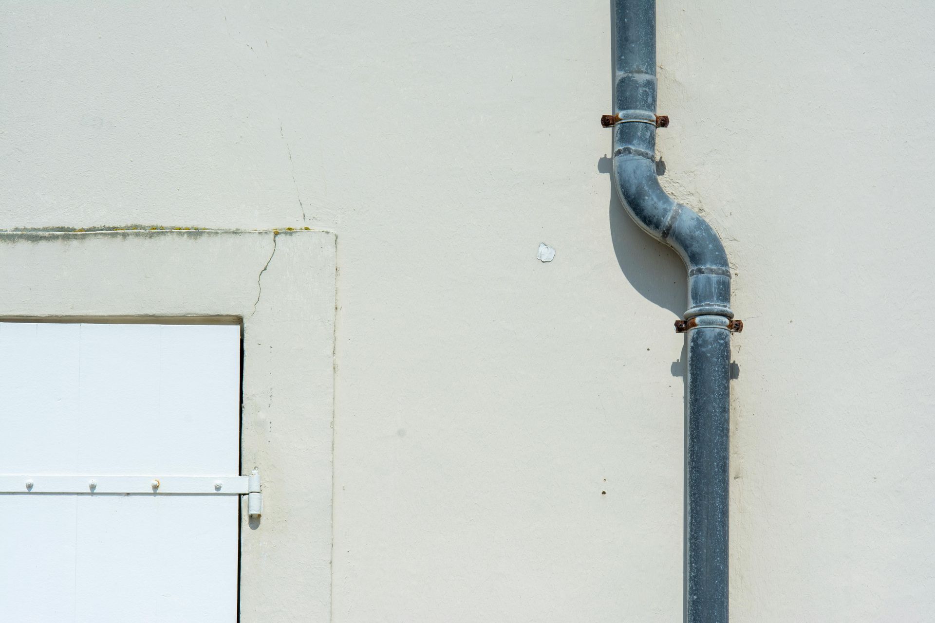 Tuyau métallique gris avec un coude courbé sur un mur extérieur blanc près du bord d'une porte