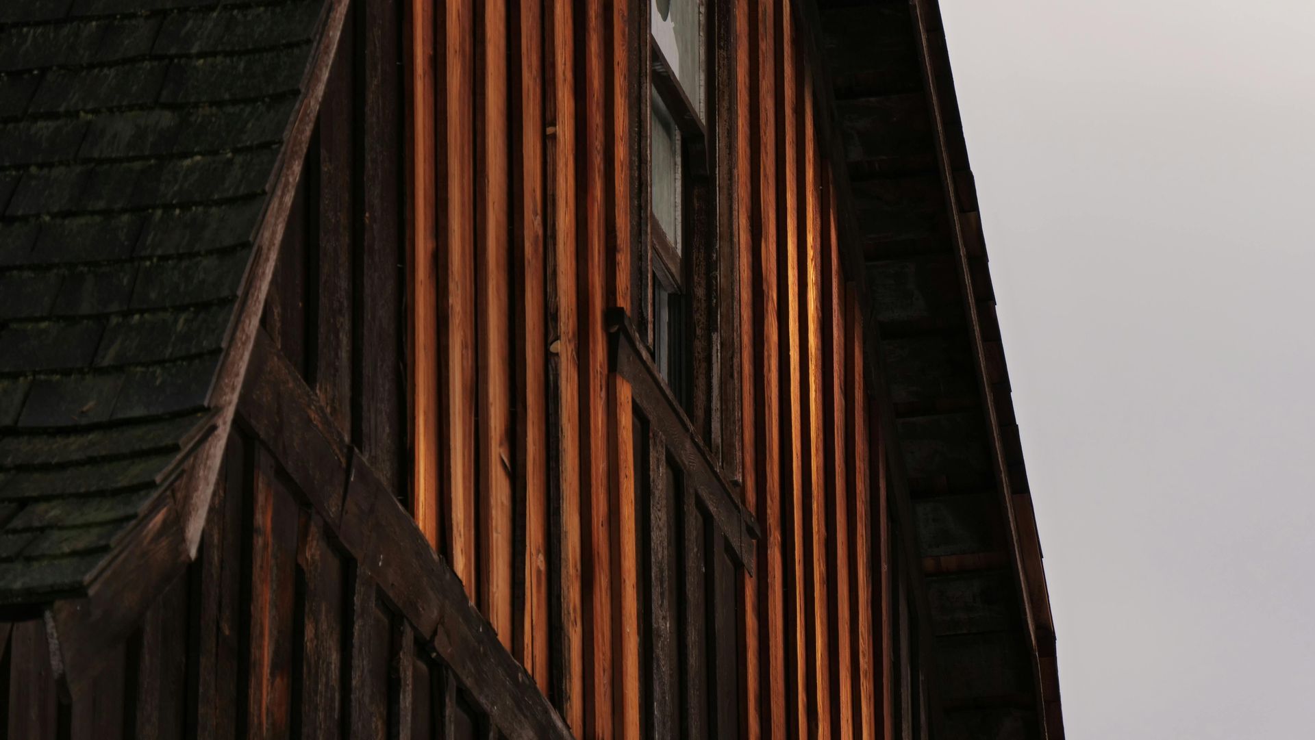 Gros plan sur la façade d'un bâtiment en bois sombre, avec un bardage vertical orange-brun et un toit en bardeaux.