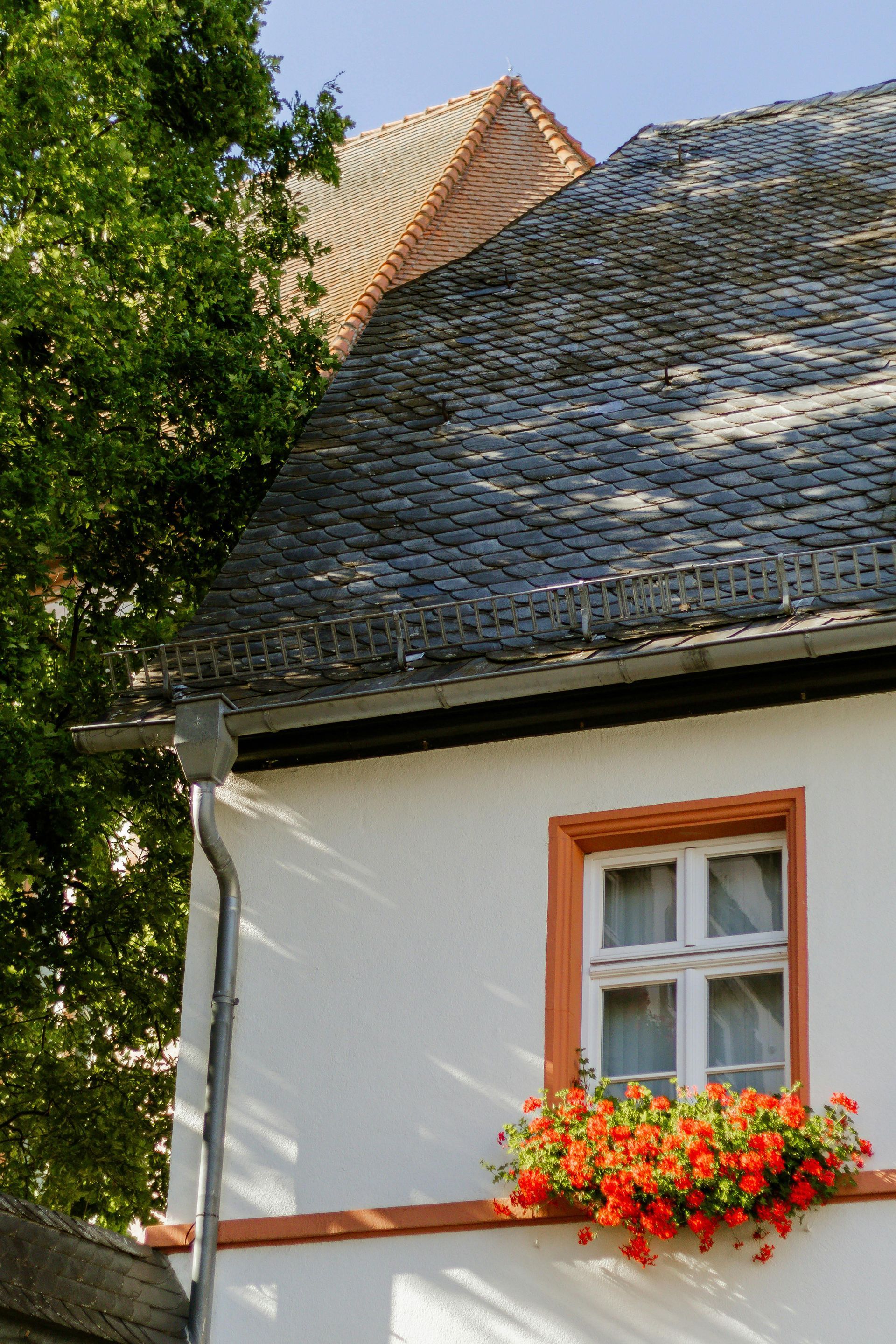 Mur blanc d'une maison avec une fenêtre à encadrement orange et une jardinière sous un toit en bardeaux gris