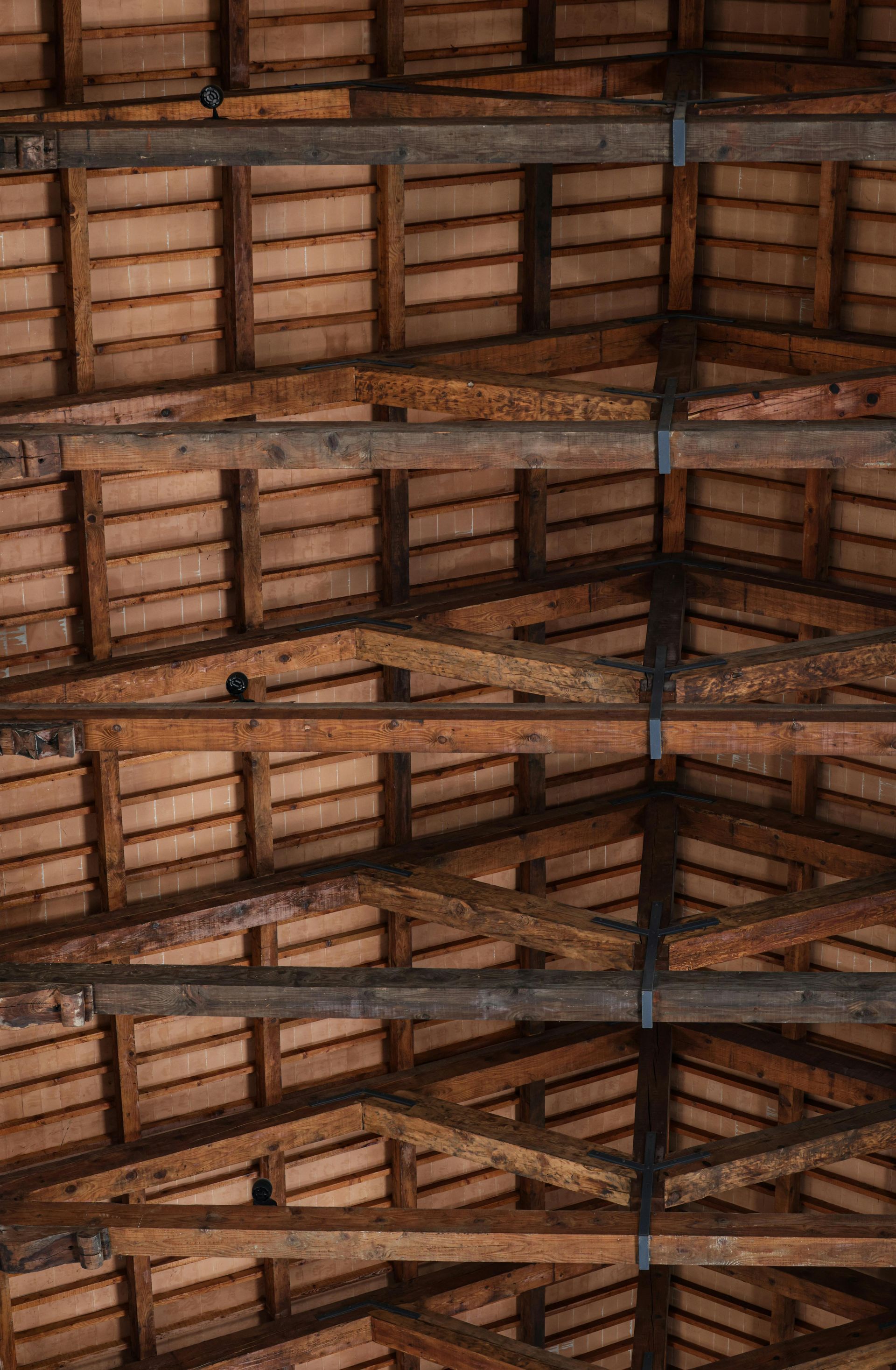 Intérieur d'une grange en bois avec poutres apparentes, chevrons et charpente de toit inclinée.