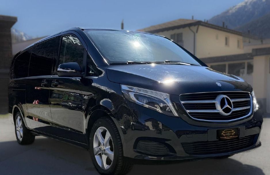 Ein schwarzer Mercedes-Transporter parkt an einem sonnigen Tag im Freien vor Häusern.