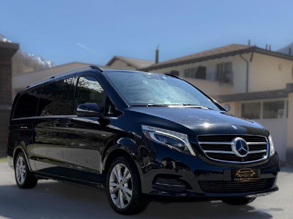 Ein schwarzer Mercedes-Transporter parkt an einem sonnigen Tag im Freien vor Wohnhäusern.