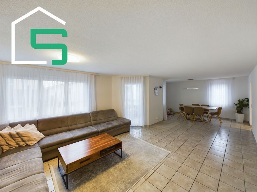 Offener Wohnbereich mit brauner Sofagarnitur, Couchtisch aus Holz und Essbereich.