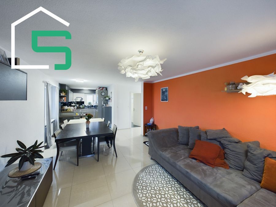 Wohnzimmer mit orangefarbener Akzentwand, grauem Sofa, schwarzem Esstisch und offener Küche.