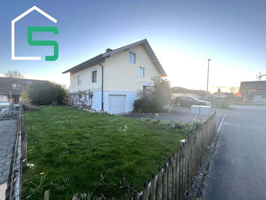 Haus mit Hof und Holzzaun, an einer Straße in der Abenddämmerung gelegen.