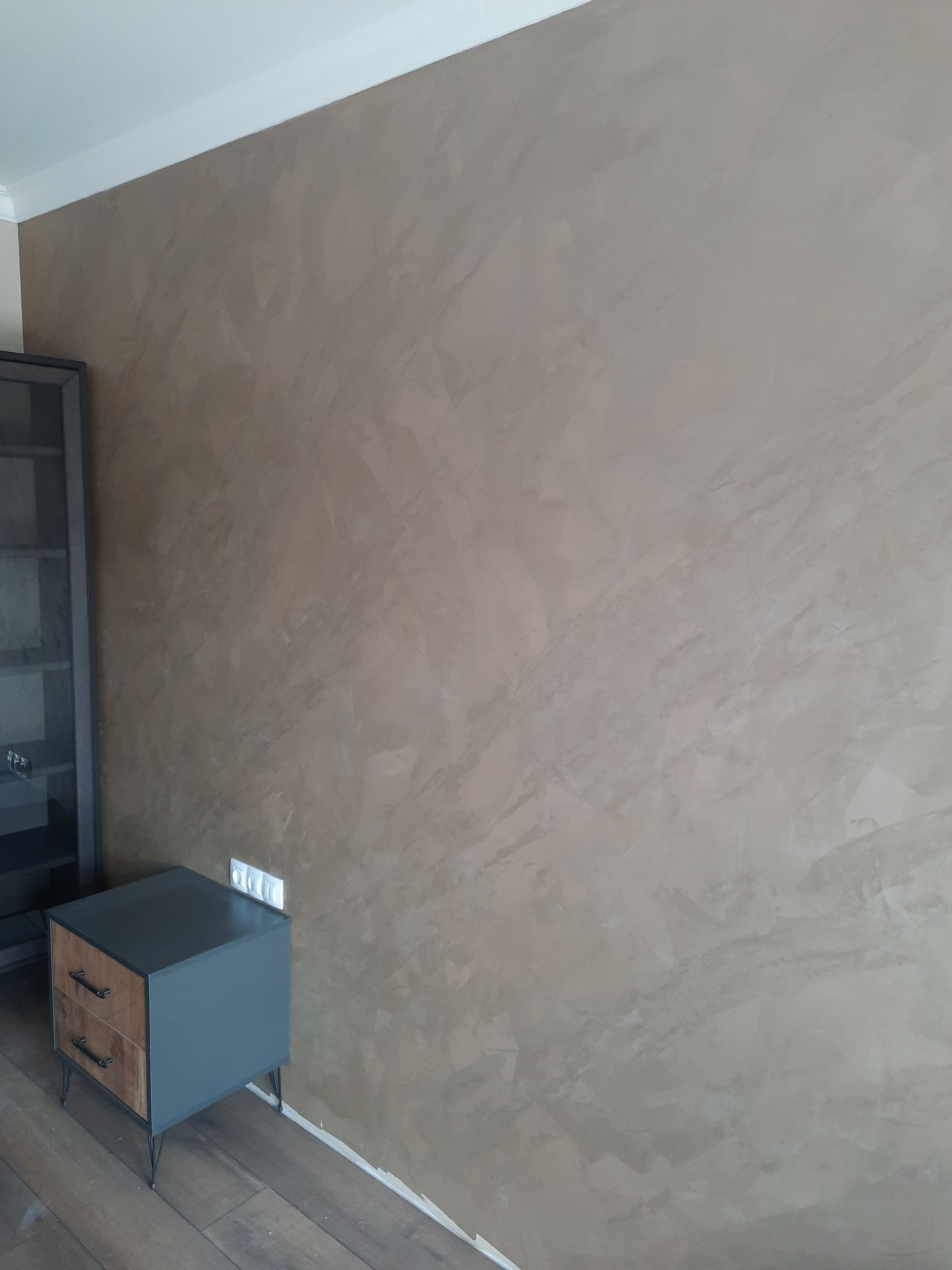 Pared marrón texturizada con armario gris oscuro y estanterías negras.