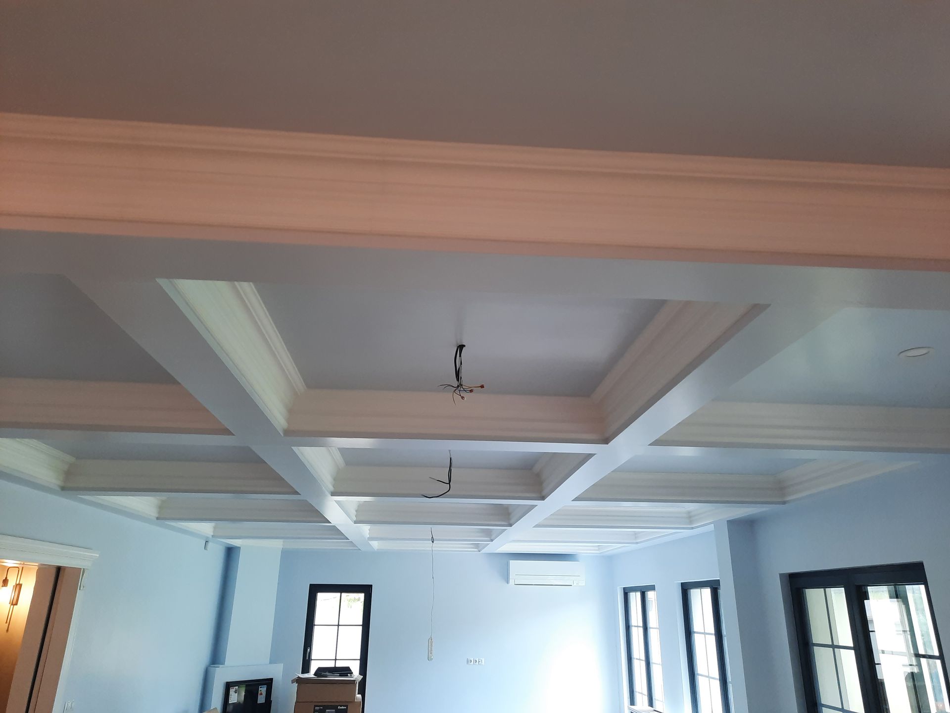 Habitación azul claro con techo artesonado blanco y marcos de ventanas negros.