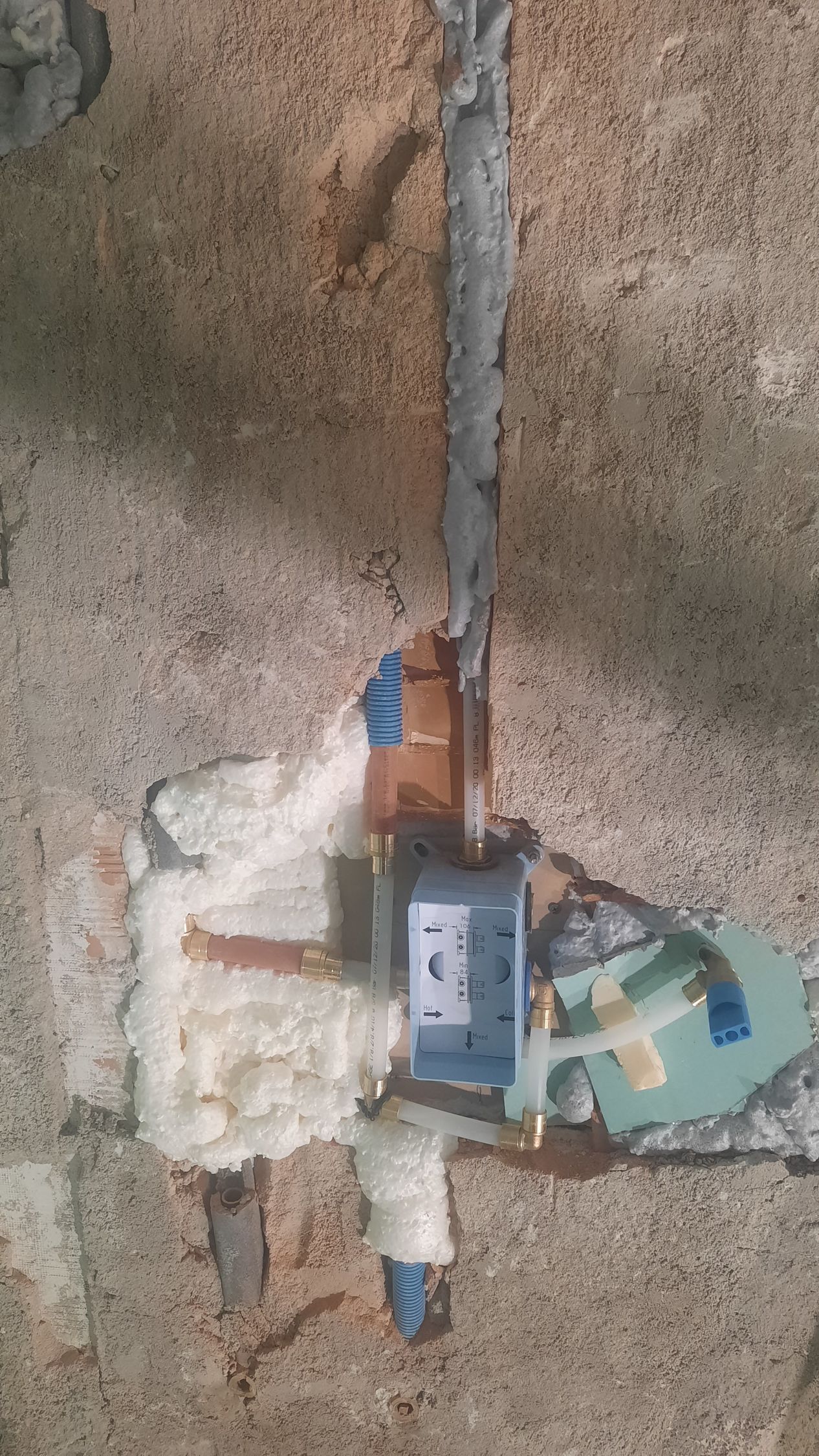 Accesorio de fontanería, parcialmente instalado, empotrado en hormigón, rodeado de aislamiento de espuma.