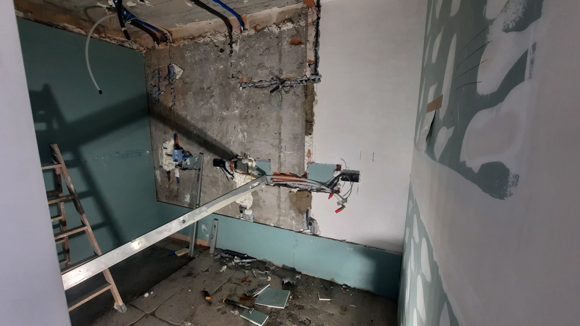 Reforma interior: pared a la vista, tuberías, escalera y pared parcialmente alicatada en una habitación.