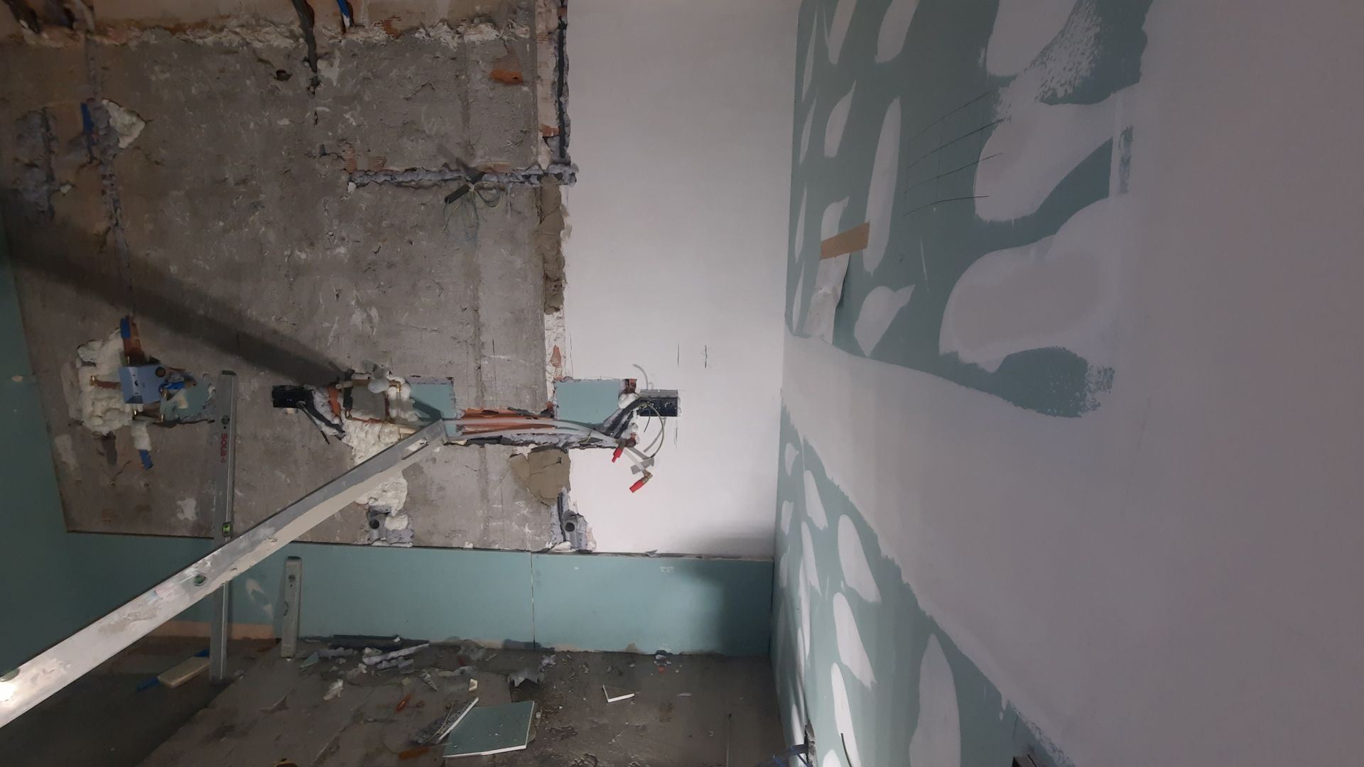 Habitación en proceso de renovación; panel de yeso a la derecha, hormigón visto a la izquierda