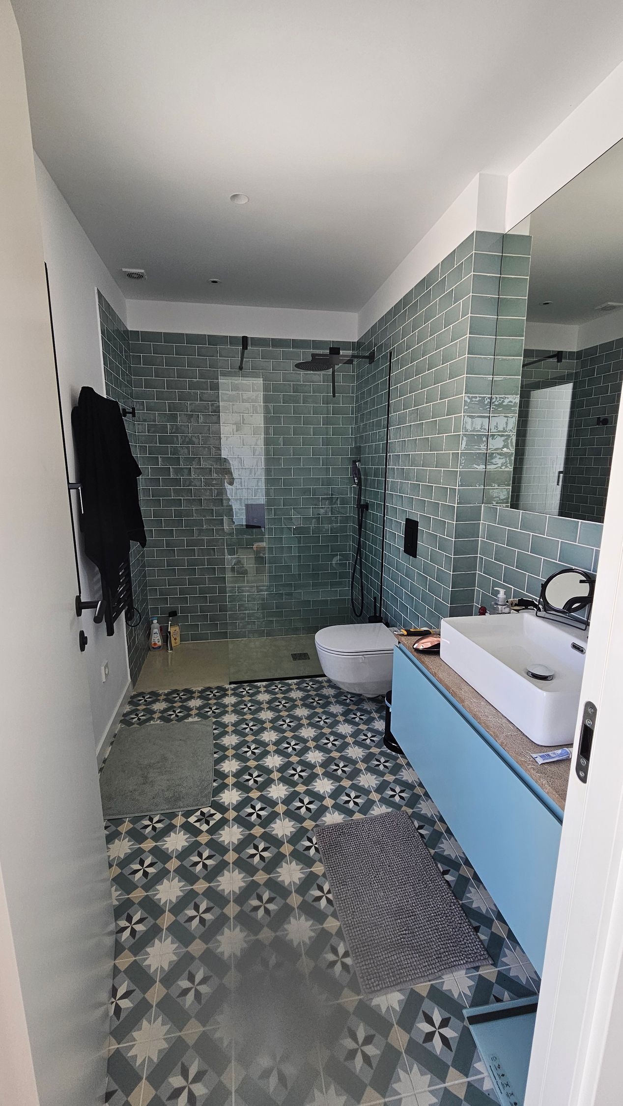 Baño con paredes alicatadas en azul, suelo estampado, lavabo blanco, inodoro y armario azul.