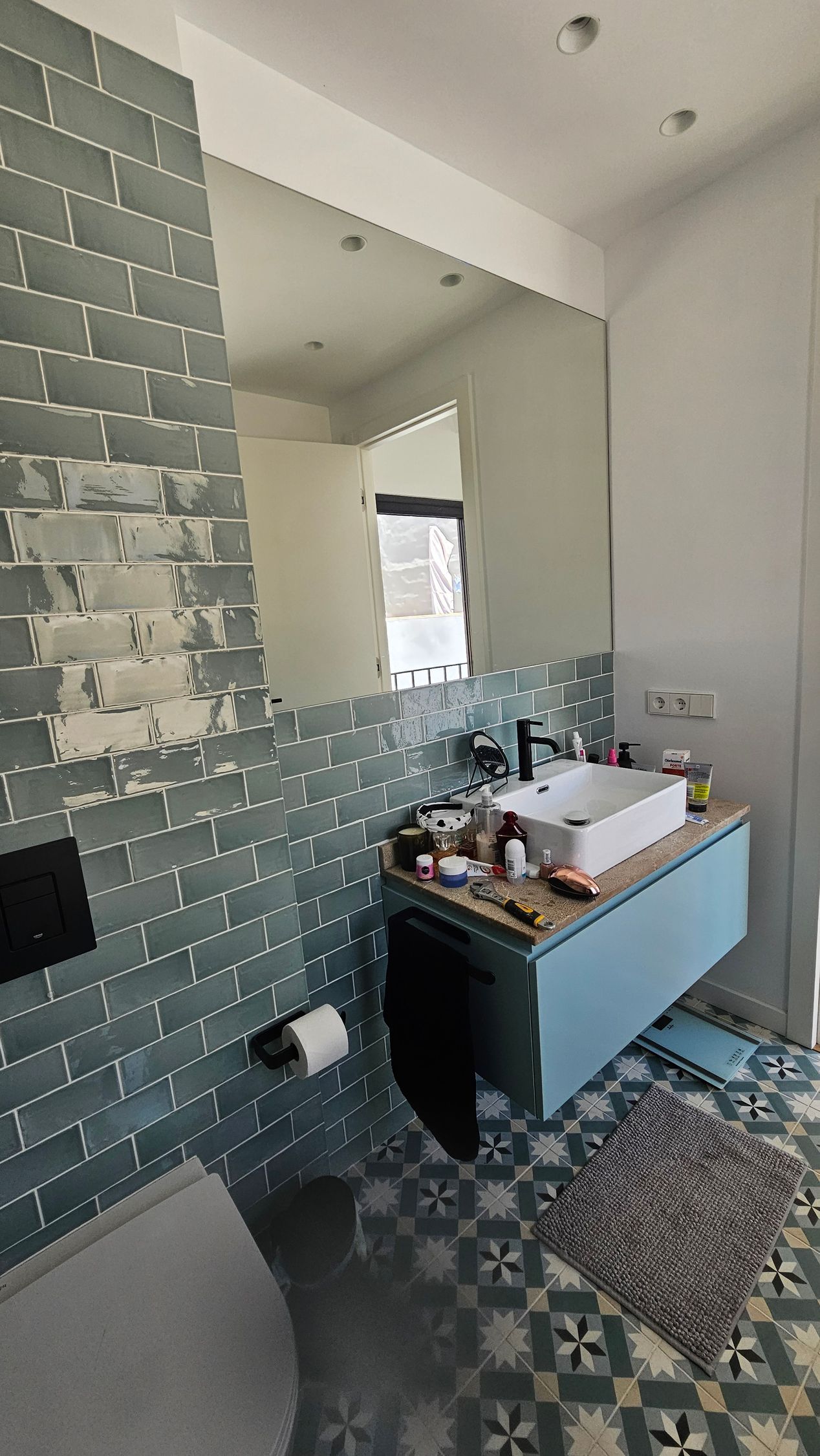 Baño con azulejos turquesa, tocador azul y un espejo grande.