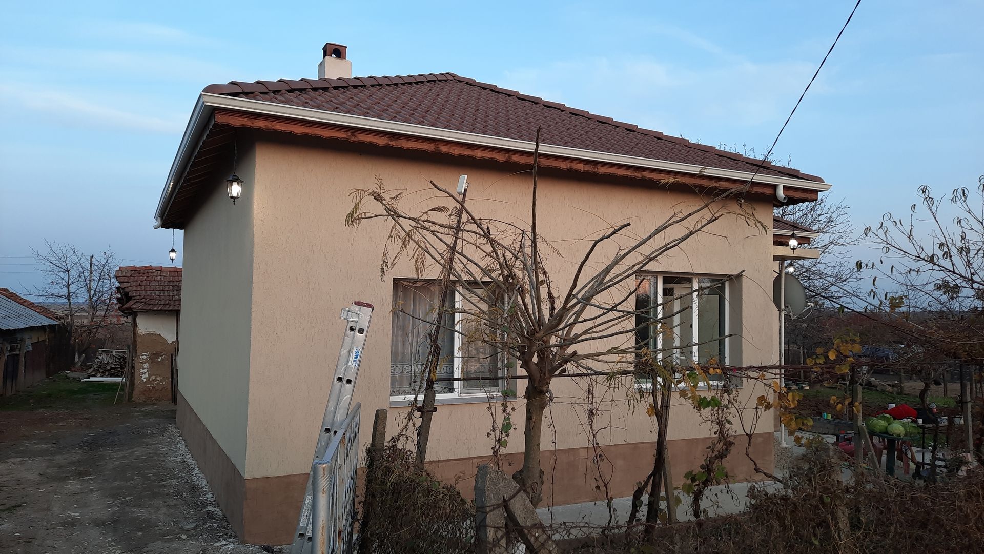Casa de estuco color canela con techo marrón y ventanas con marcos blancos, rodeada de árboles desnudos bajo un cielo azul.