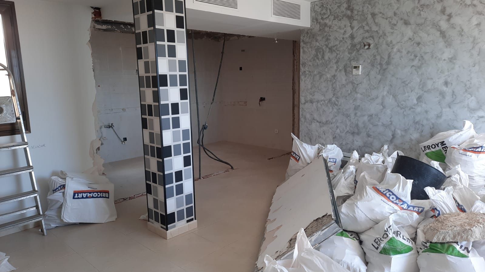 Interior en construcción; sacos de material, columna alicatada, cableado a la vista.