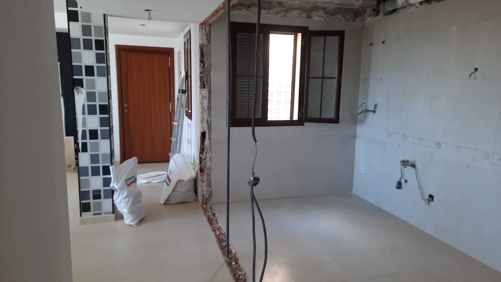 Interior de una habitación en reforma. Pared, ventana y cableado a la vista. Paredes blancas, suelo claro.