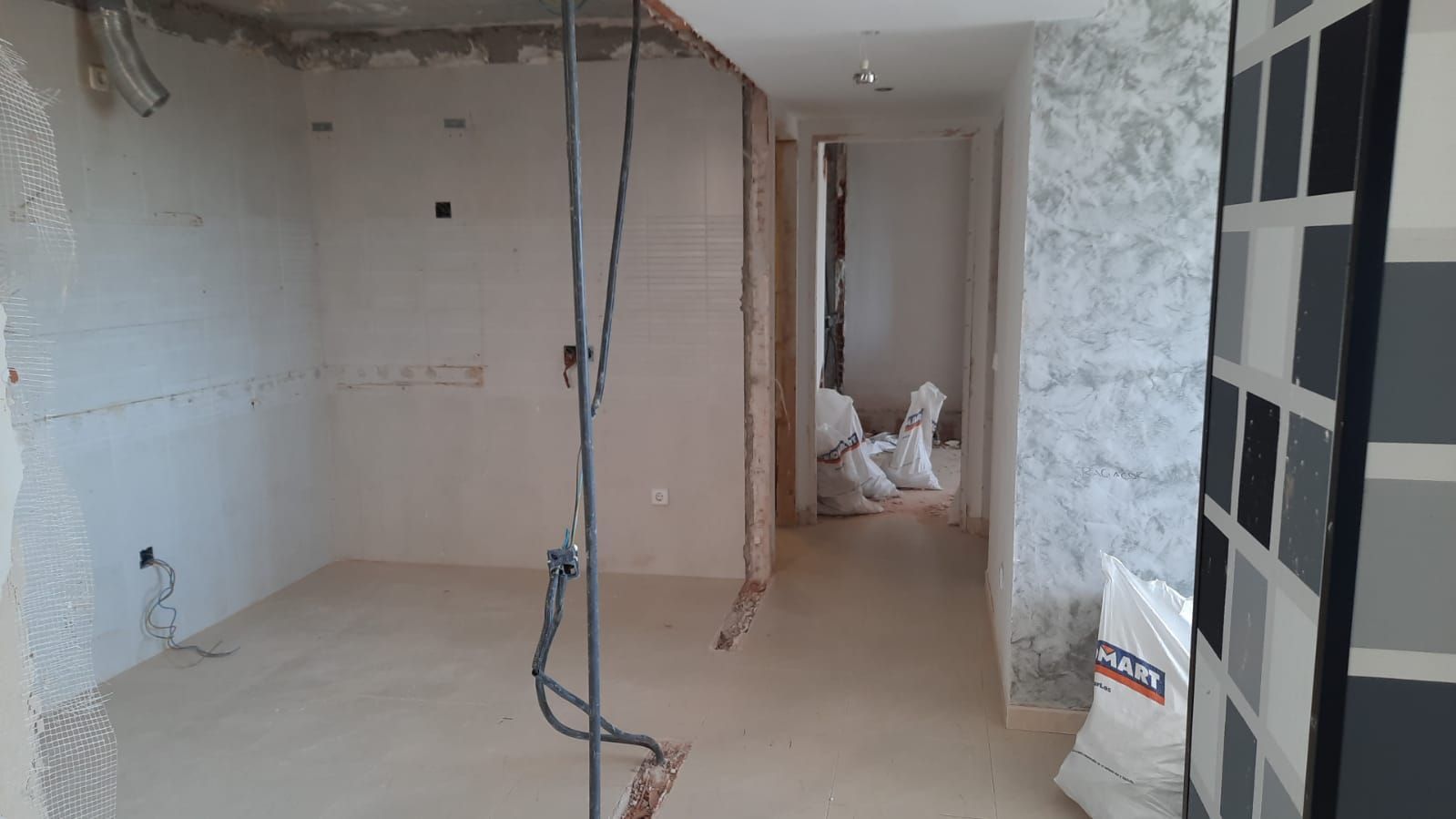 Habitación interior en obras, con cableado a la vista, paredes de cemento y bolsas de escombros en la entrada.
