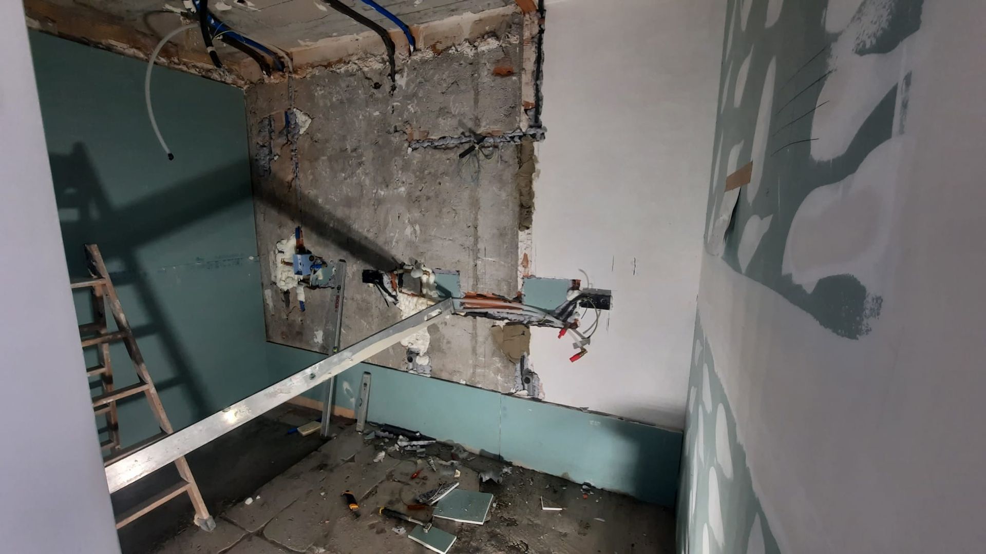 Habitación en construcción con cableado y tuberías a la vista, y paredes parcialmente demolidas; escalera visible.