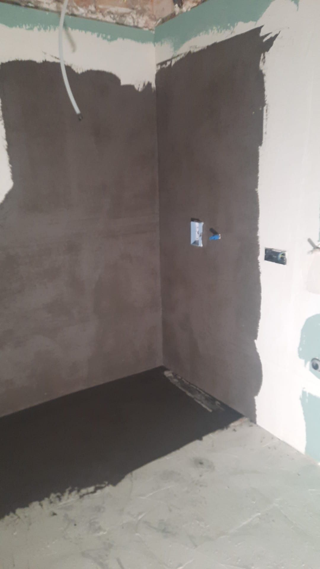 Esquina interior con paredes y suelo de yeso gris oscuro, con dos tomas de corriente visibles.