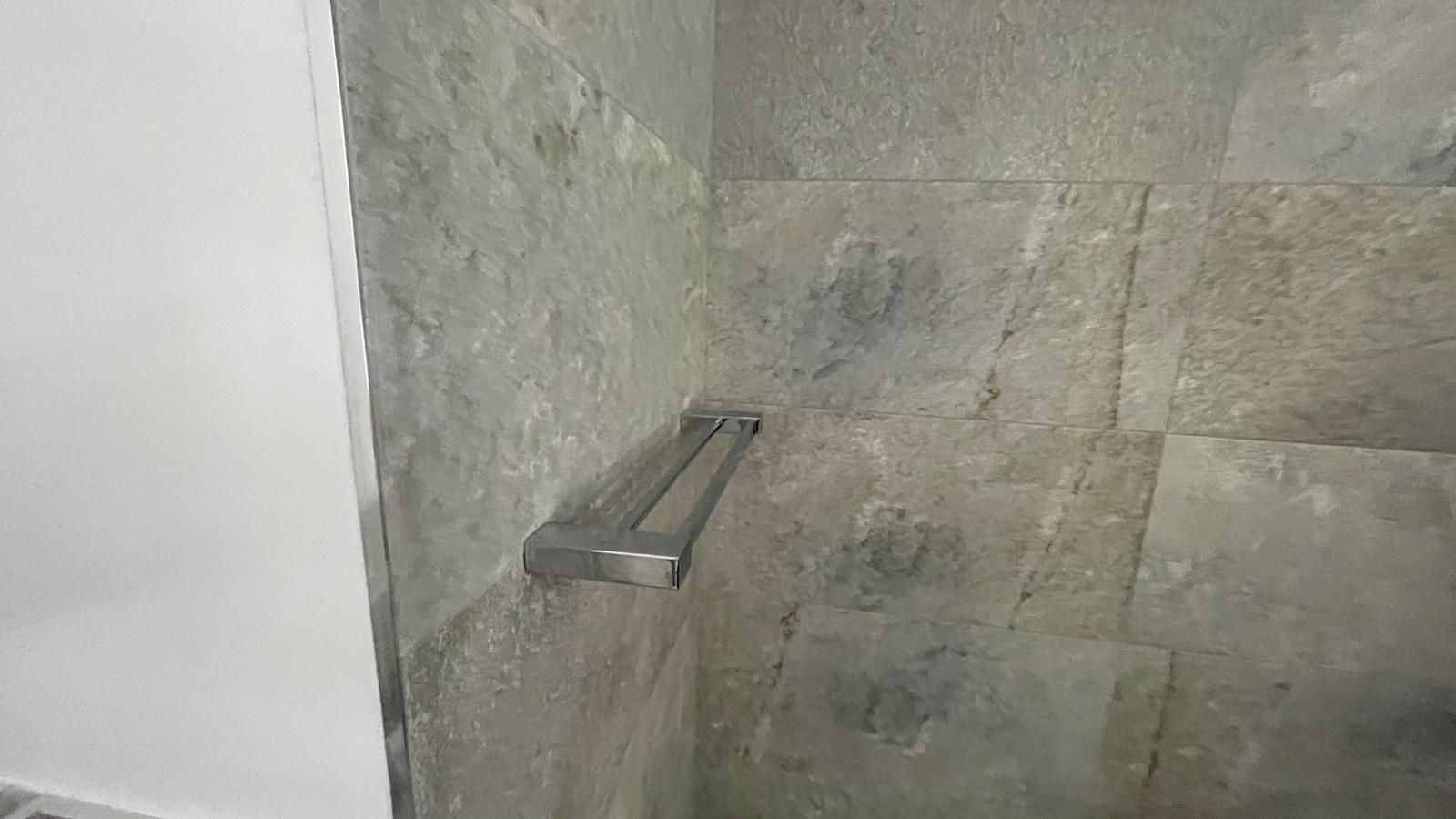 Toallero sobre pared de piedra gris en una esquina del baño.