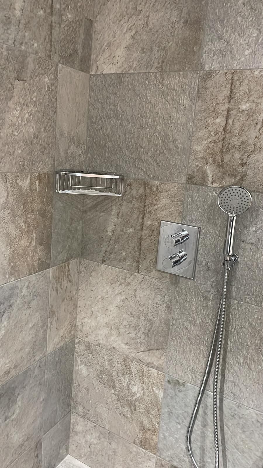 Interior de ducha con azulejos de piedra, repisa, cabezal de ducha y controles de temperatura.