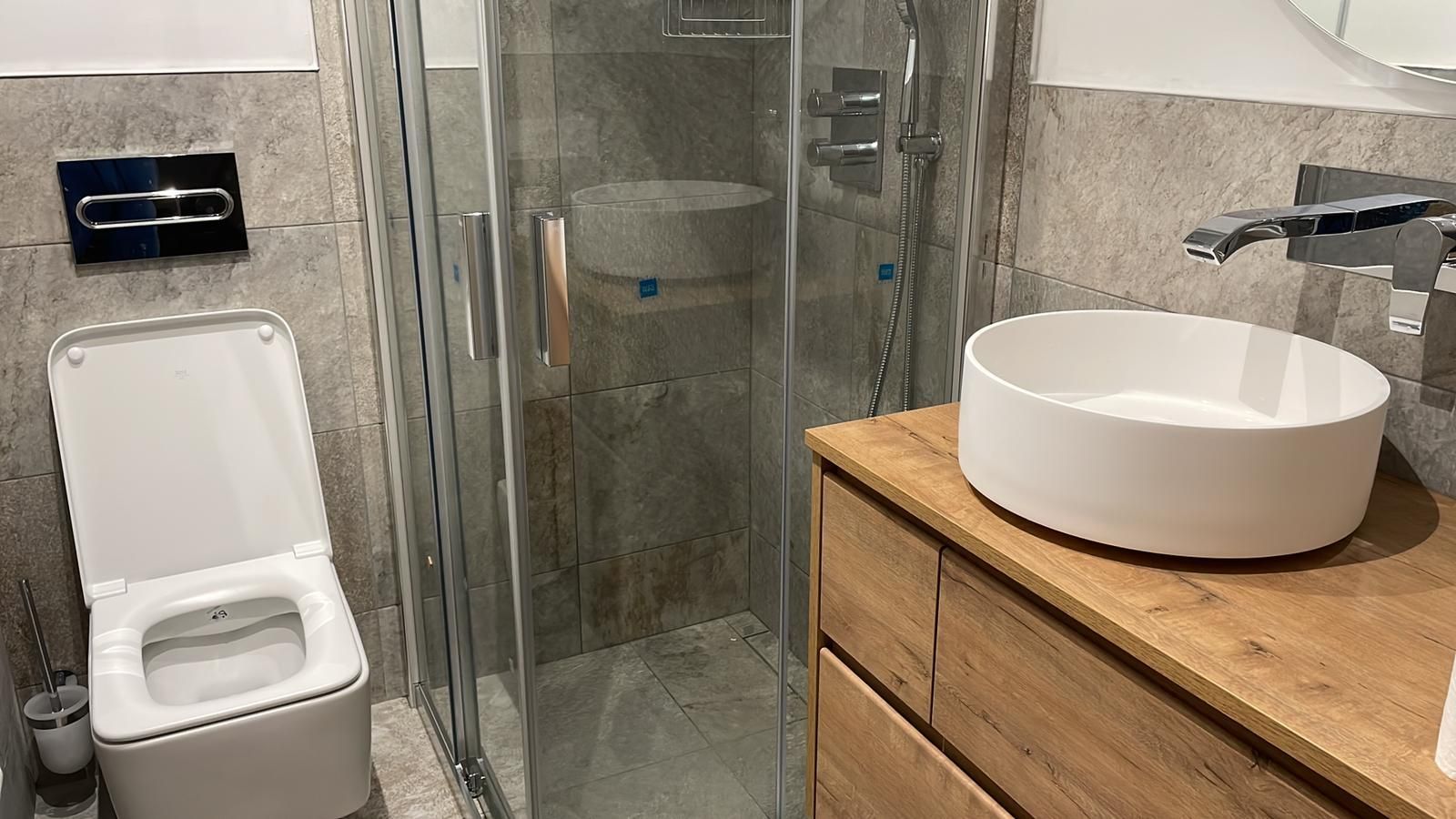 Baño pequeño con inodoro, ducha y lavabo sobre un mueble de madera.