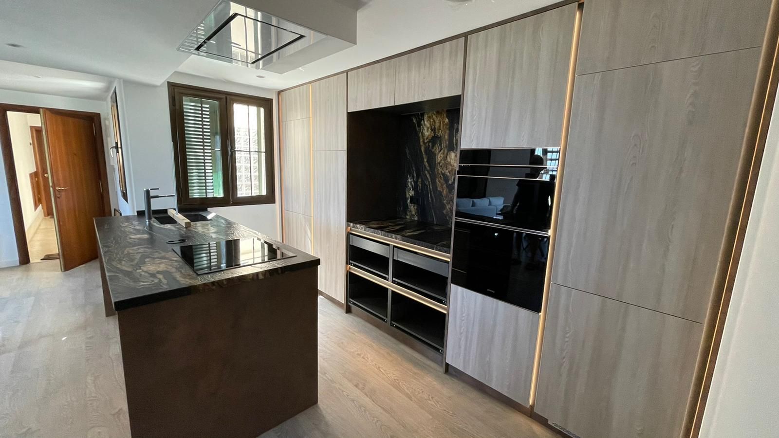 Cocina moderna con gabinetes de madera clara, encimeras negras e isla.