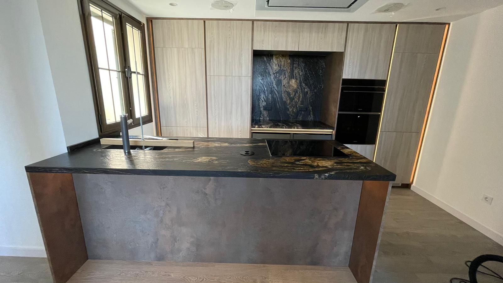 Cocina moderna con isla de piedra, armarios de madera y salpicadero negro.