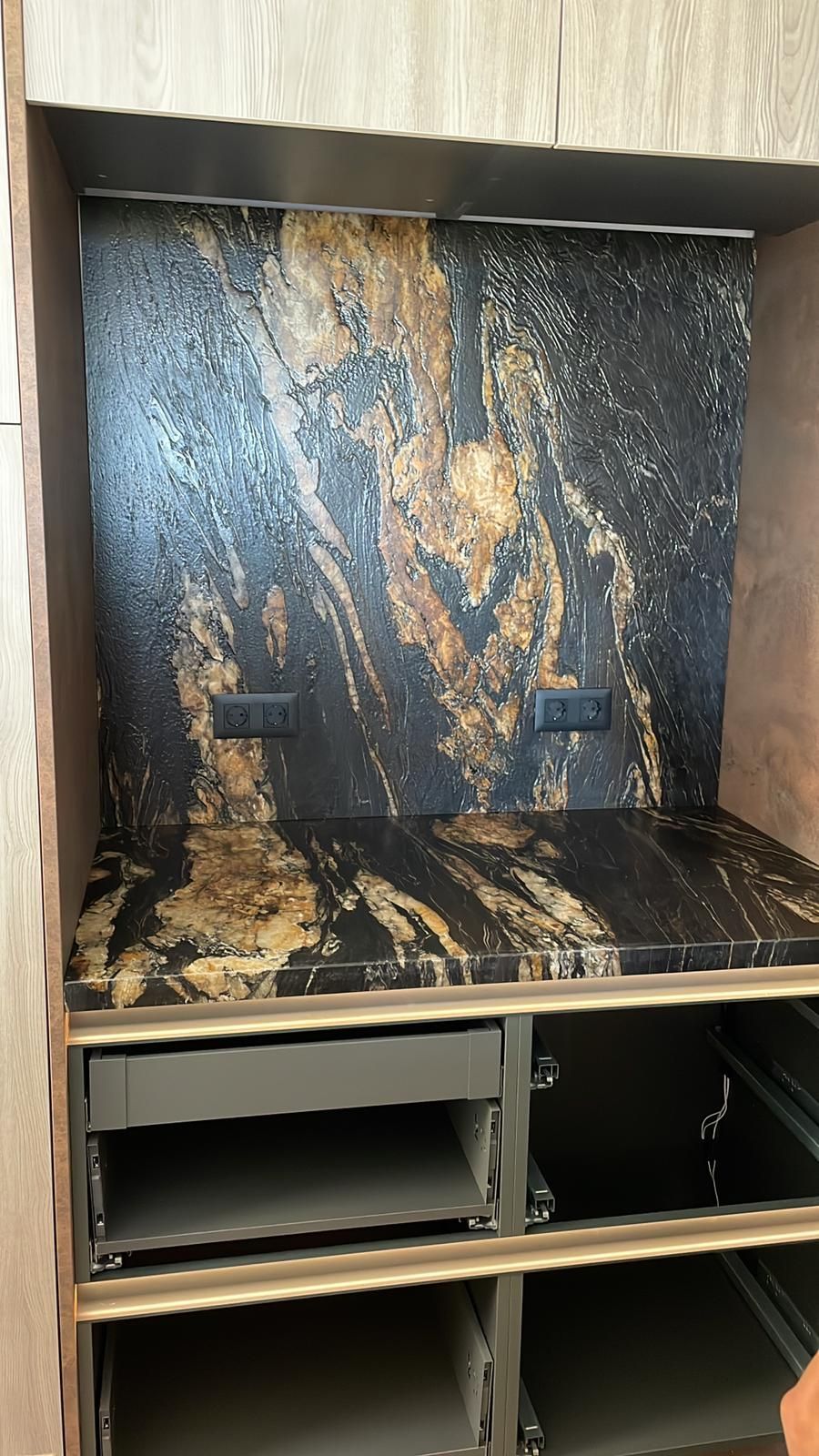 Armario empotrado con encimera y salpicadero de granito negro y dorado, que alberga enchufes, con espacio de