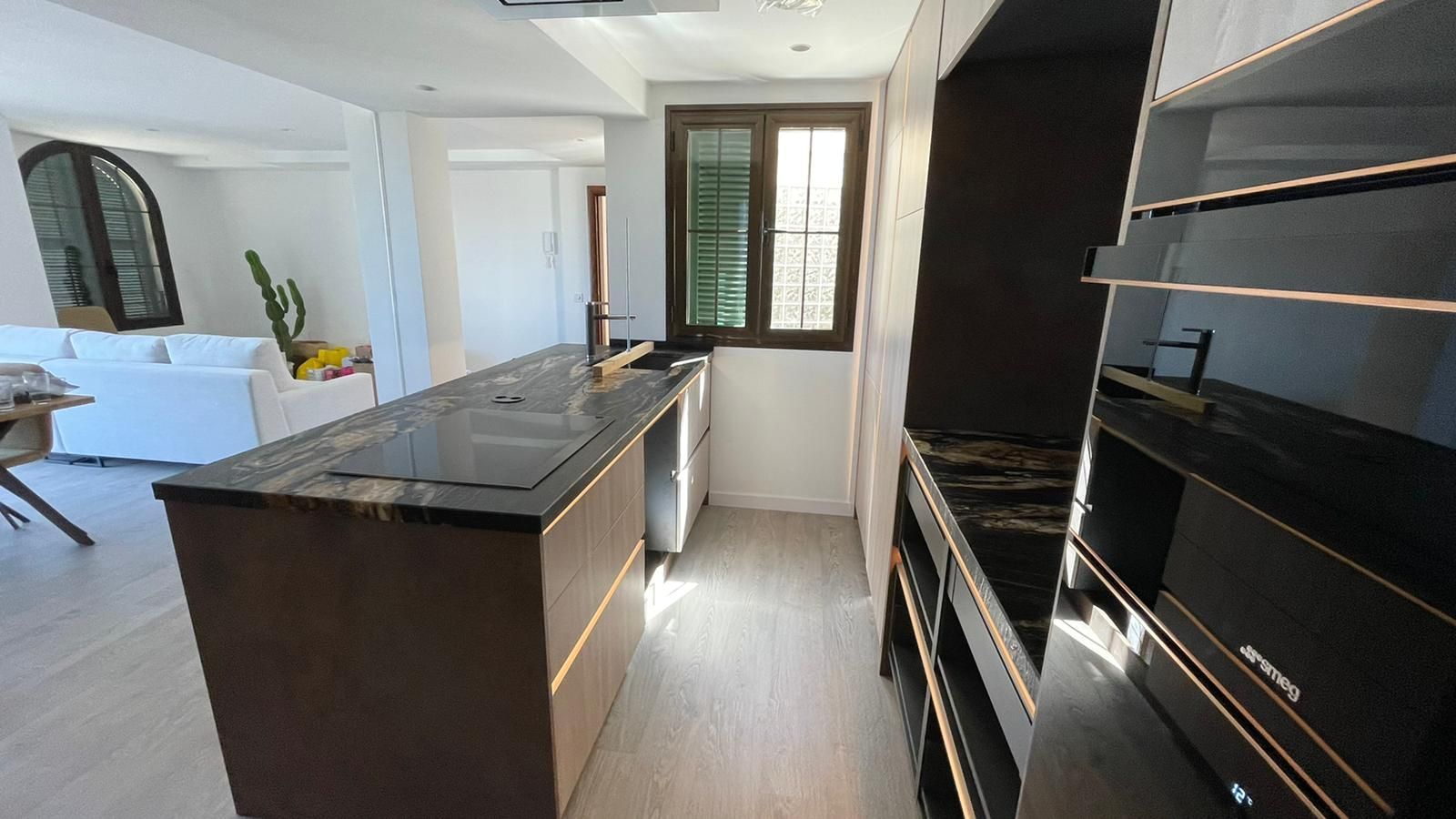 Cocina moderna con gabinetes oscuros, encimera negra y ventana.