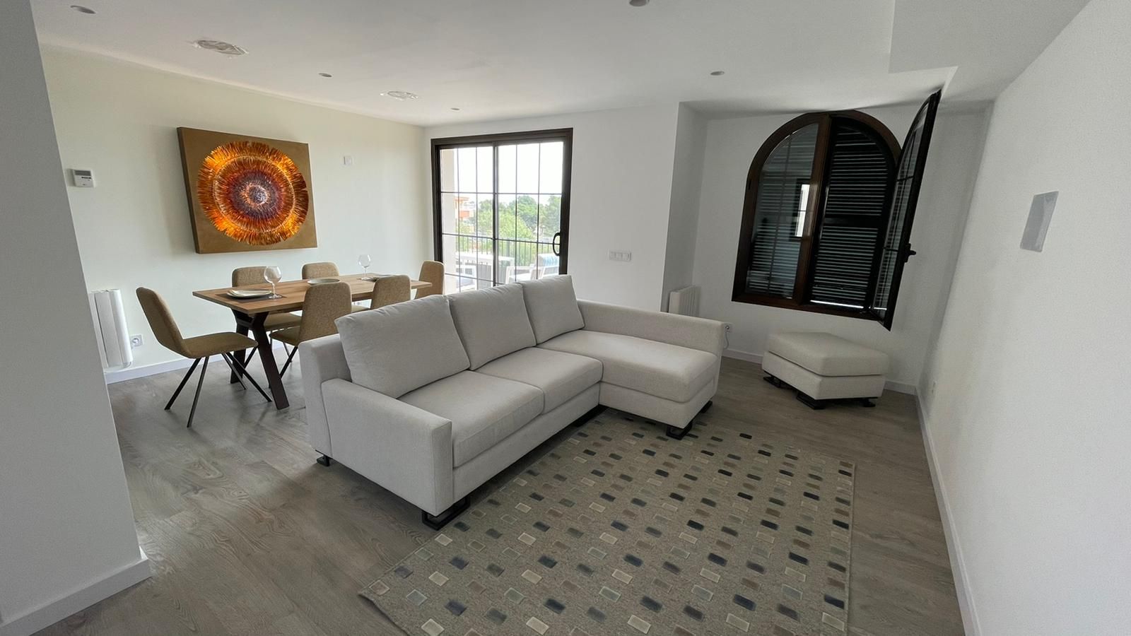 Sala de estar con sofá seccional blanco, mesa de comedor y ventana arqueada con contraventanas.