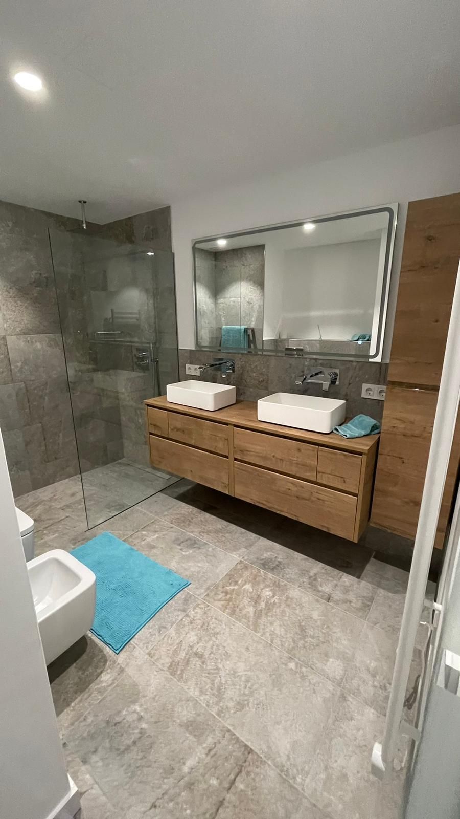 Baño moderno con tocador flotante de madera, dos lavabos, espejo grande, ducha de cristal,