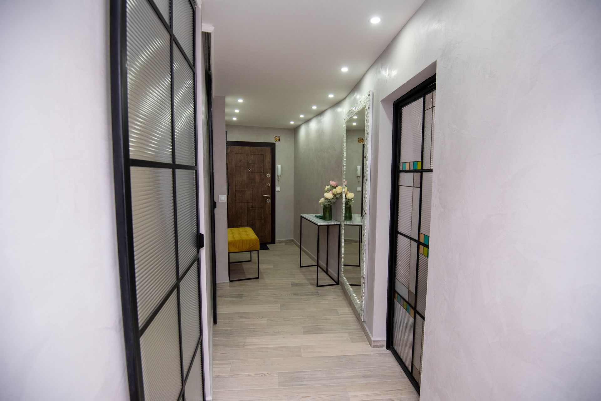 Pasillo con puertas de rejilla negra, pared curva con espejo, mesa consola y puerta de madera.