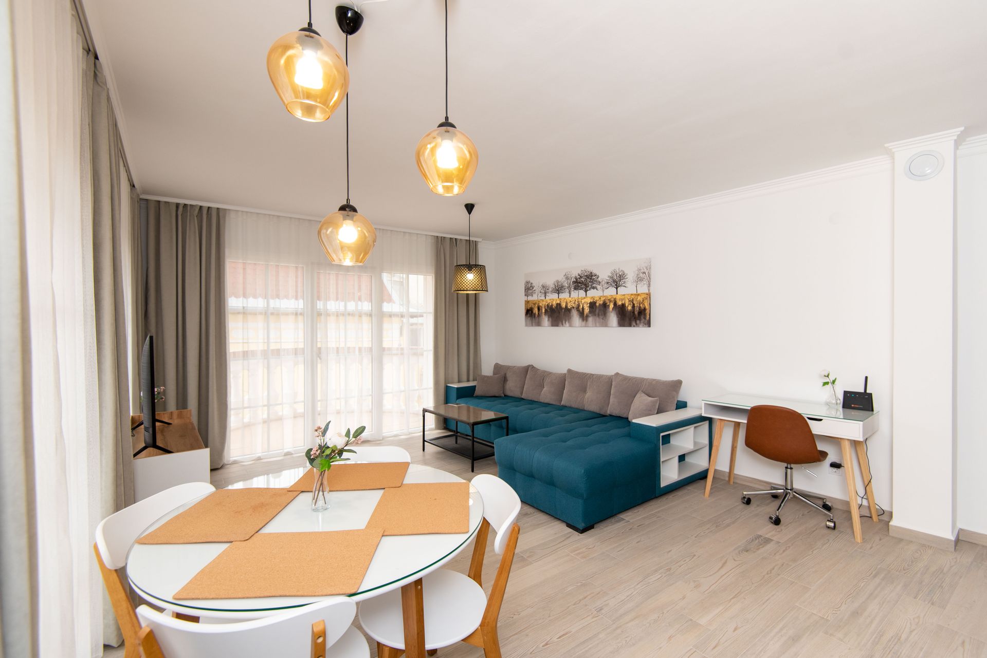 Sala de estar con mesa de comedor redonda, sofá seccional color verde azulado y lámparas colgantes.