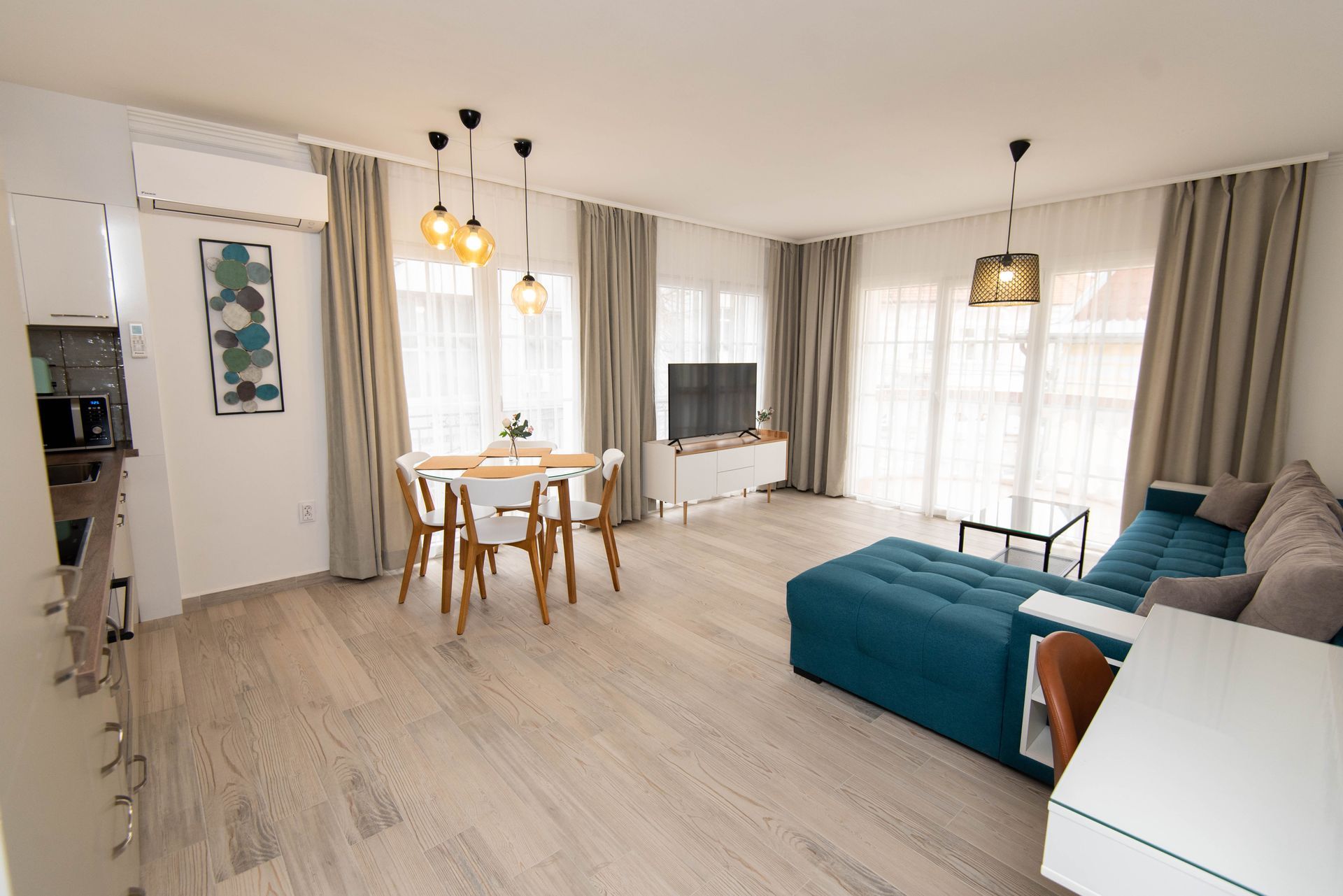 Amplia sala de estar con sofá color verde azulado, mesa de comedor y televisor. 