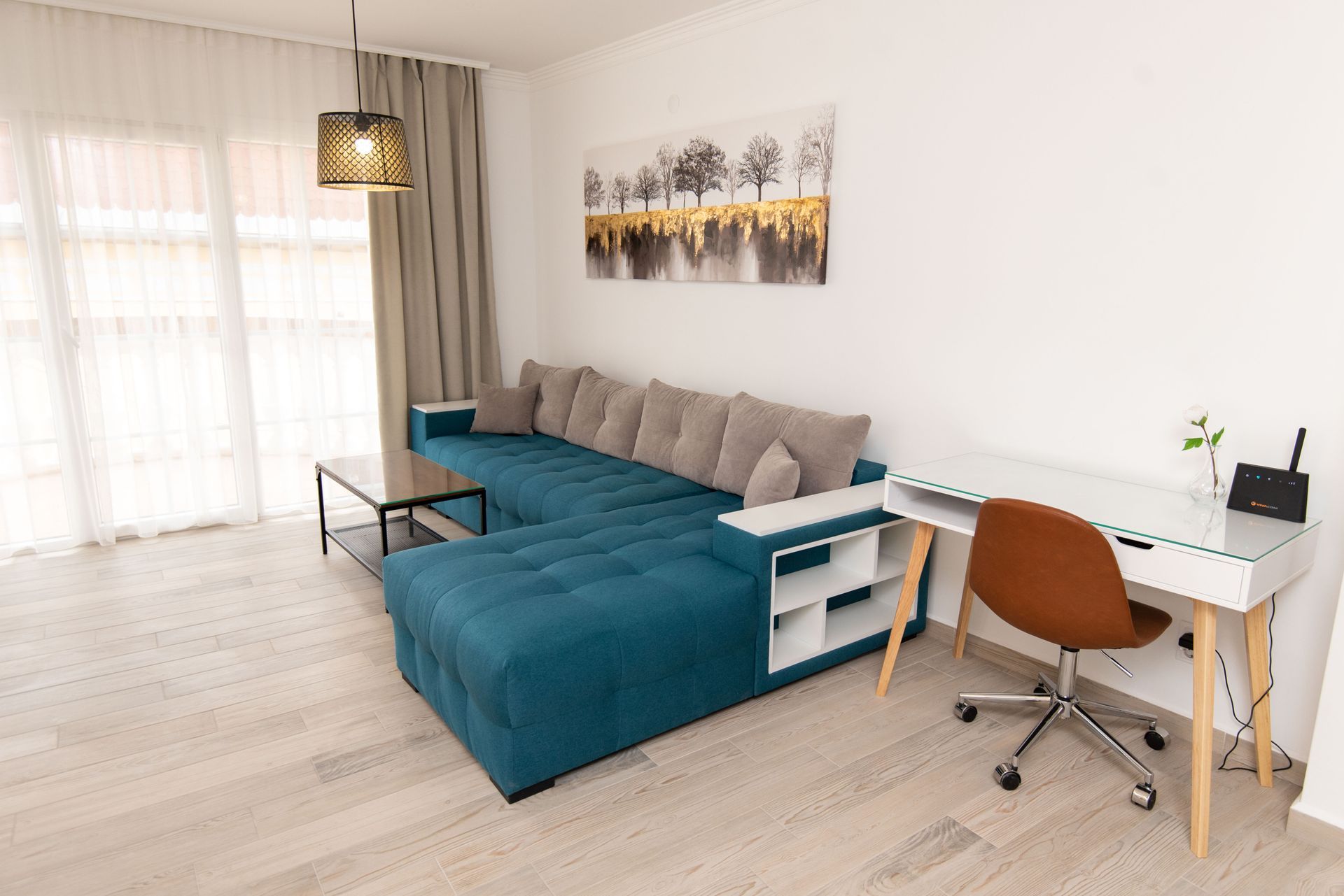 Sala de estar con sofá seccional turquesa, escritorio blanco, silla marrón y obras de arte.