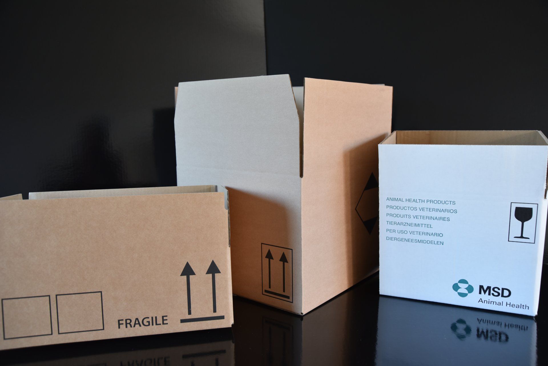 Trois boîtes en carton de tailles différentes, deux brunes, une blanche, avec étiquettes et symboles d'expédition.