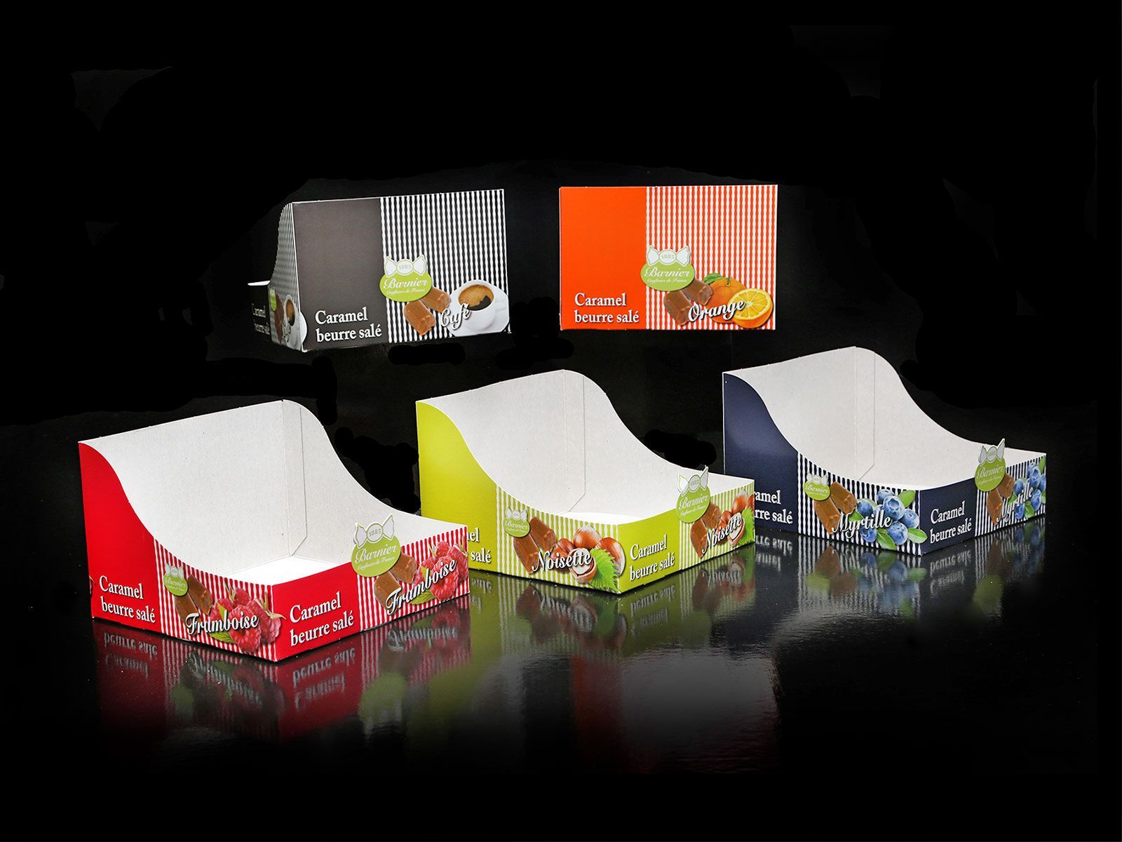 Assortiment de boîtes présentoirs colorées, chacune avec une face avant incurvée, mettant en valeur des produits alimentaires, sur fond noir.