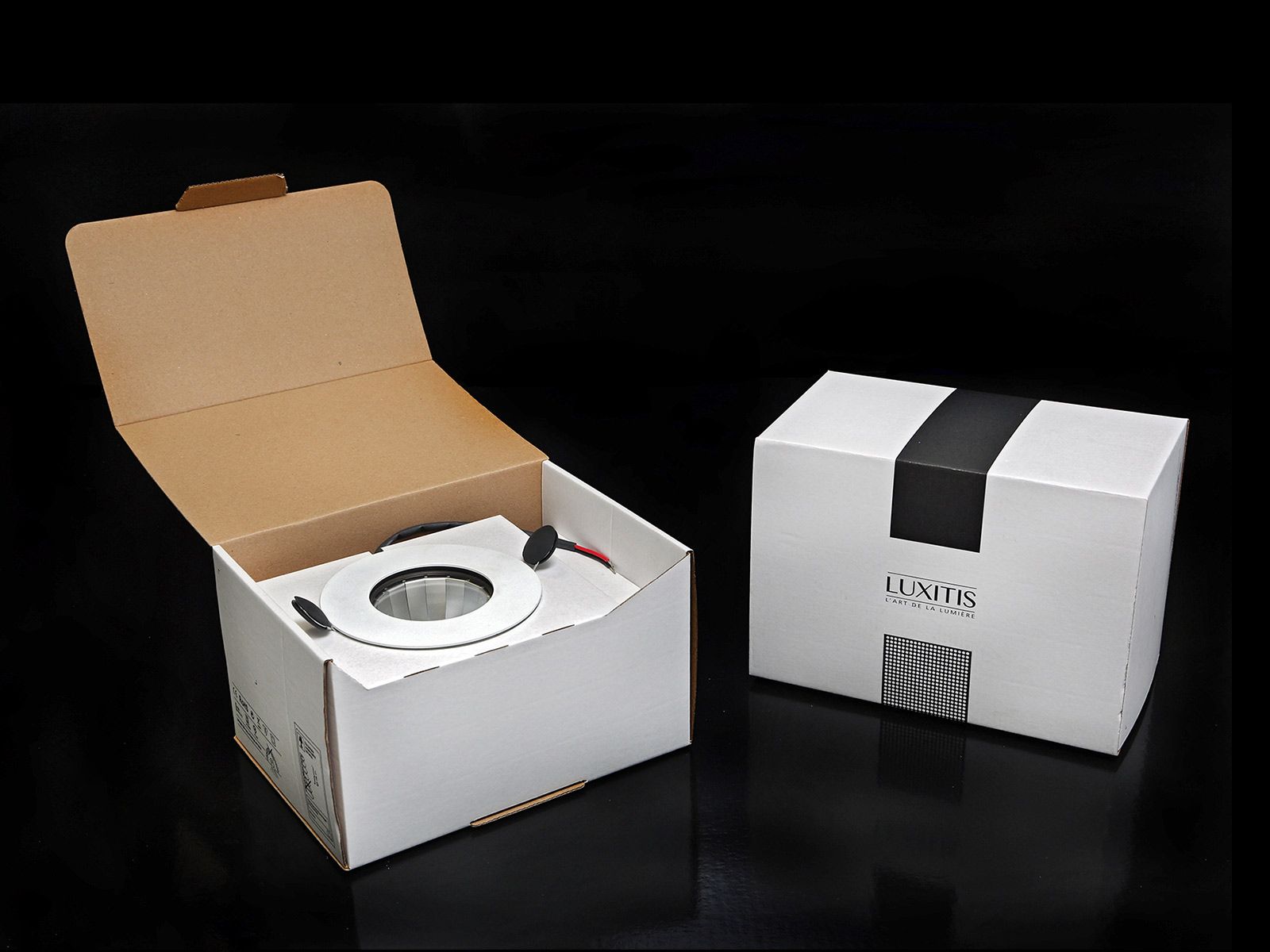 Deux boîtes blanches contenant le produit, l'une ouverte laissant apparaître un appareil, l'autre fermée par un bandeau noir.