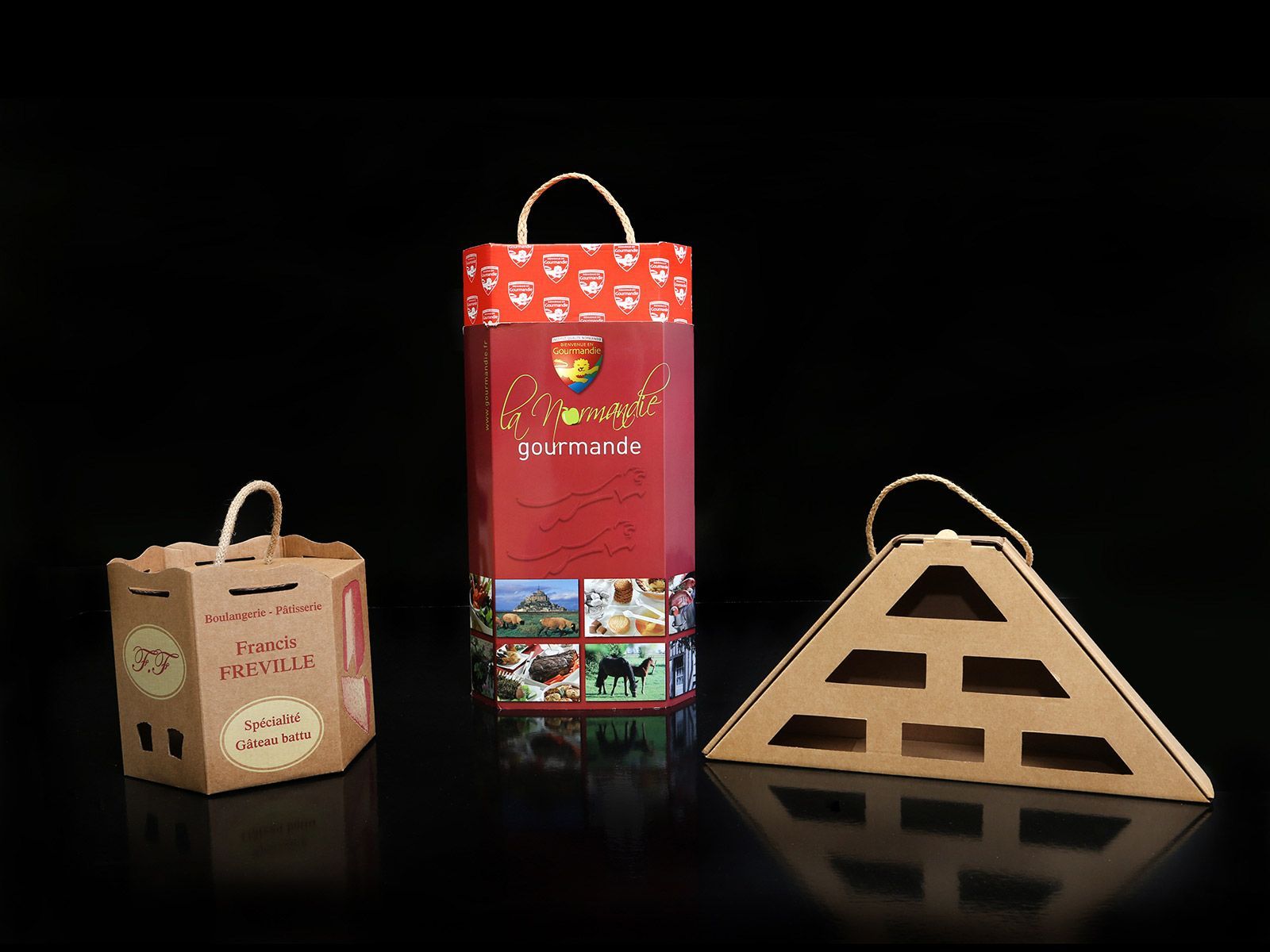 Trois boîtes cadeaux en carton avec poignées. L'une est cylindrique, l'autre carrée et la dernière en forme de pyramide.