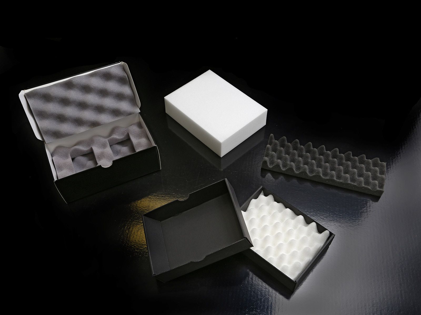 Divers inserts et boîtes en mousse, de formes et de couleurs différentes, sur fond noir.