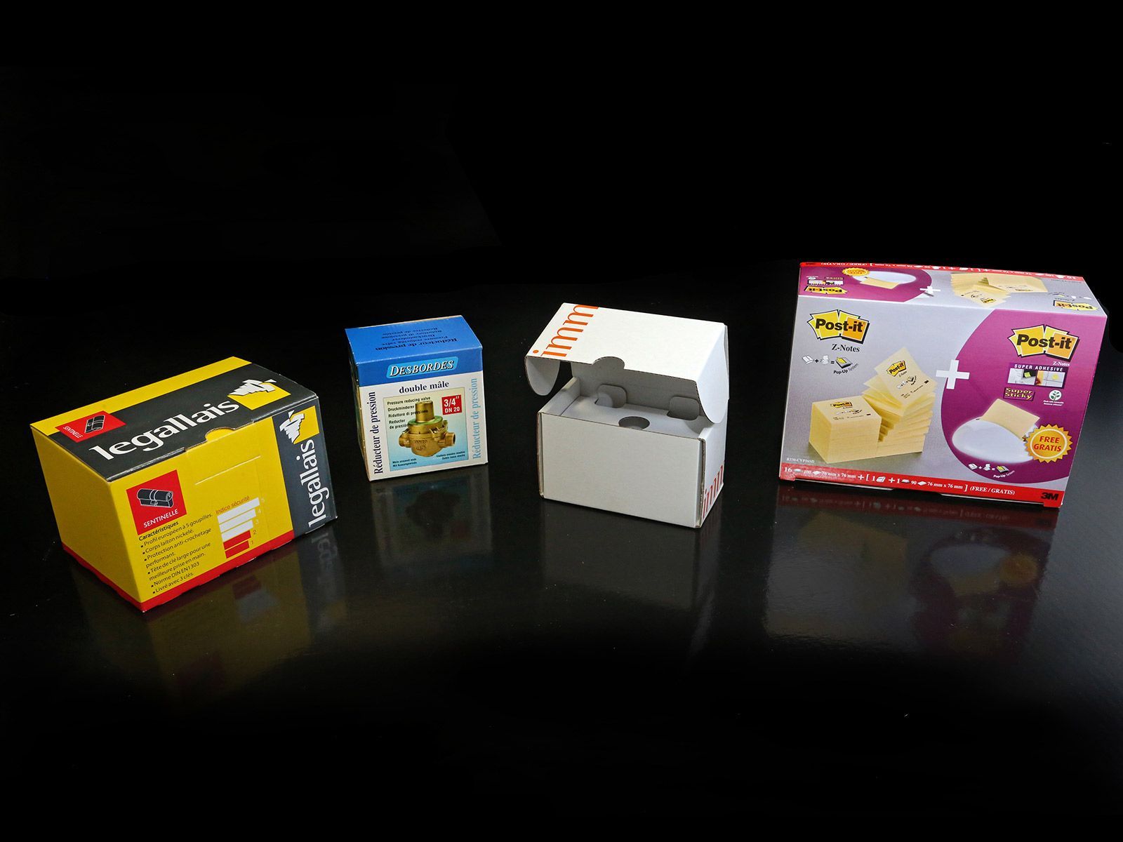 Quatre boîtes de Post-it® sur fond noir. Les boîtes sont jaunes, bleues, blanches et rouges, avec des motifs variés.