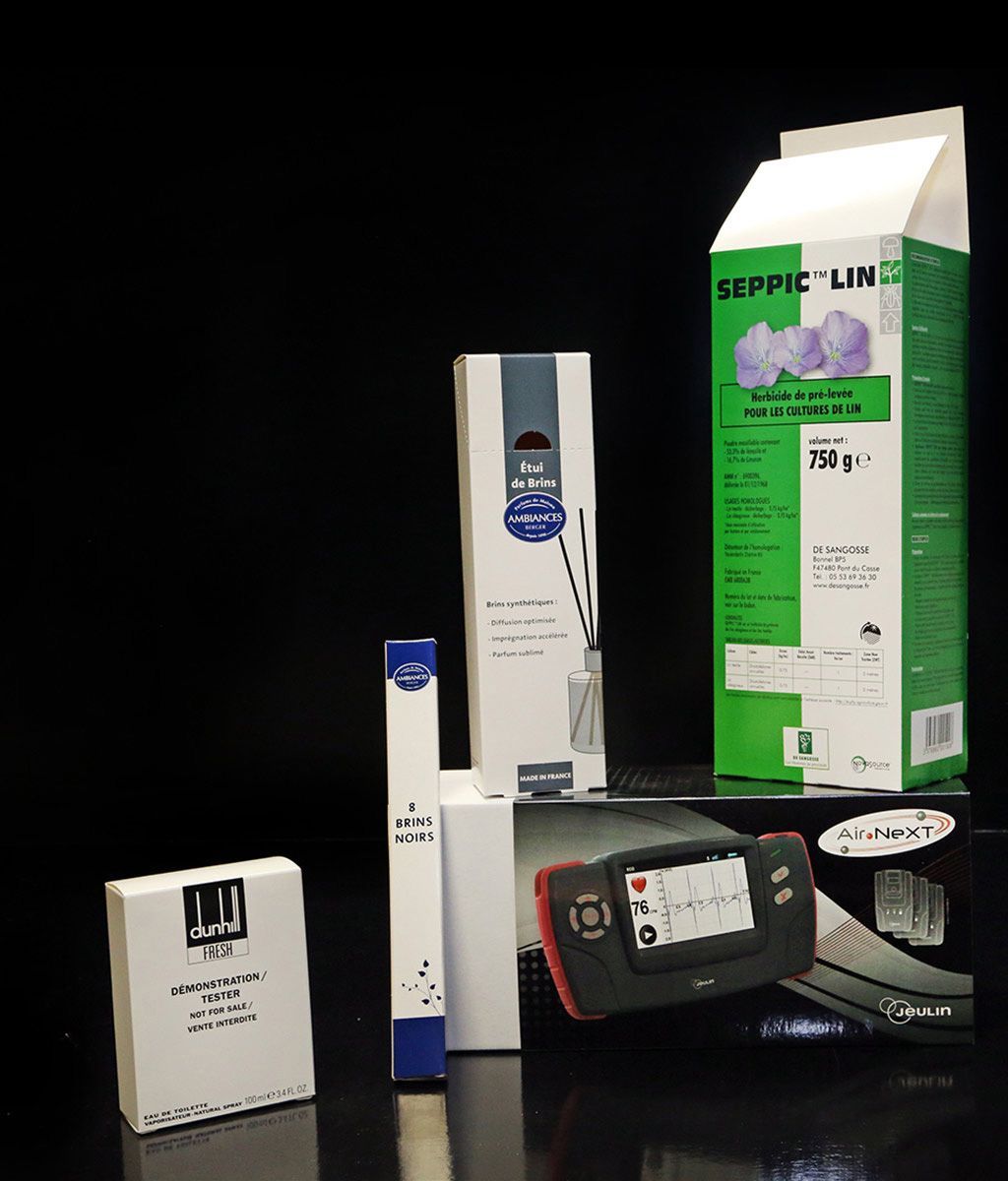 Produits sur surface noire : diverses boîtes, un appareil et des emballages avec du texte vert.