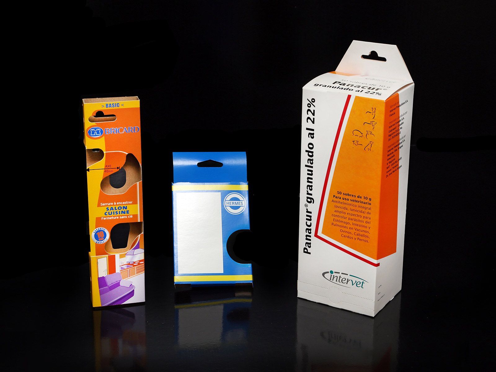 Trois boîtes de produits avec languettes de suspension sur une surface noire.